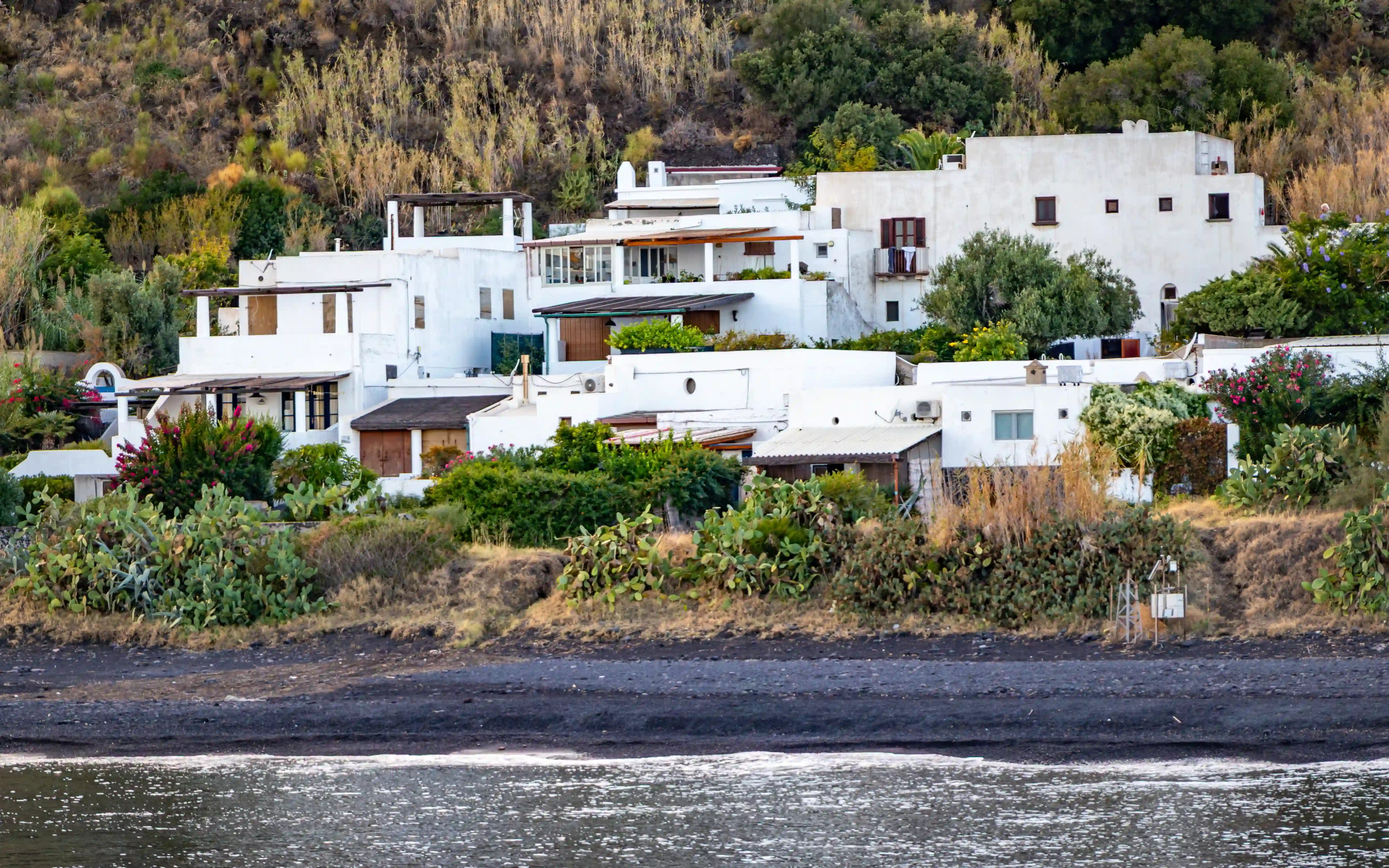 White houses with flat roofs and greenery along a dark shoreline.