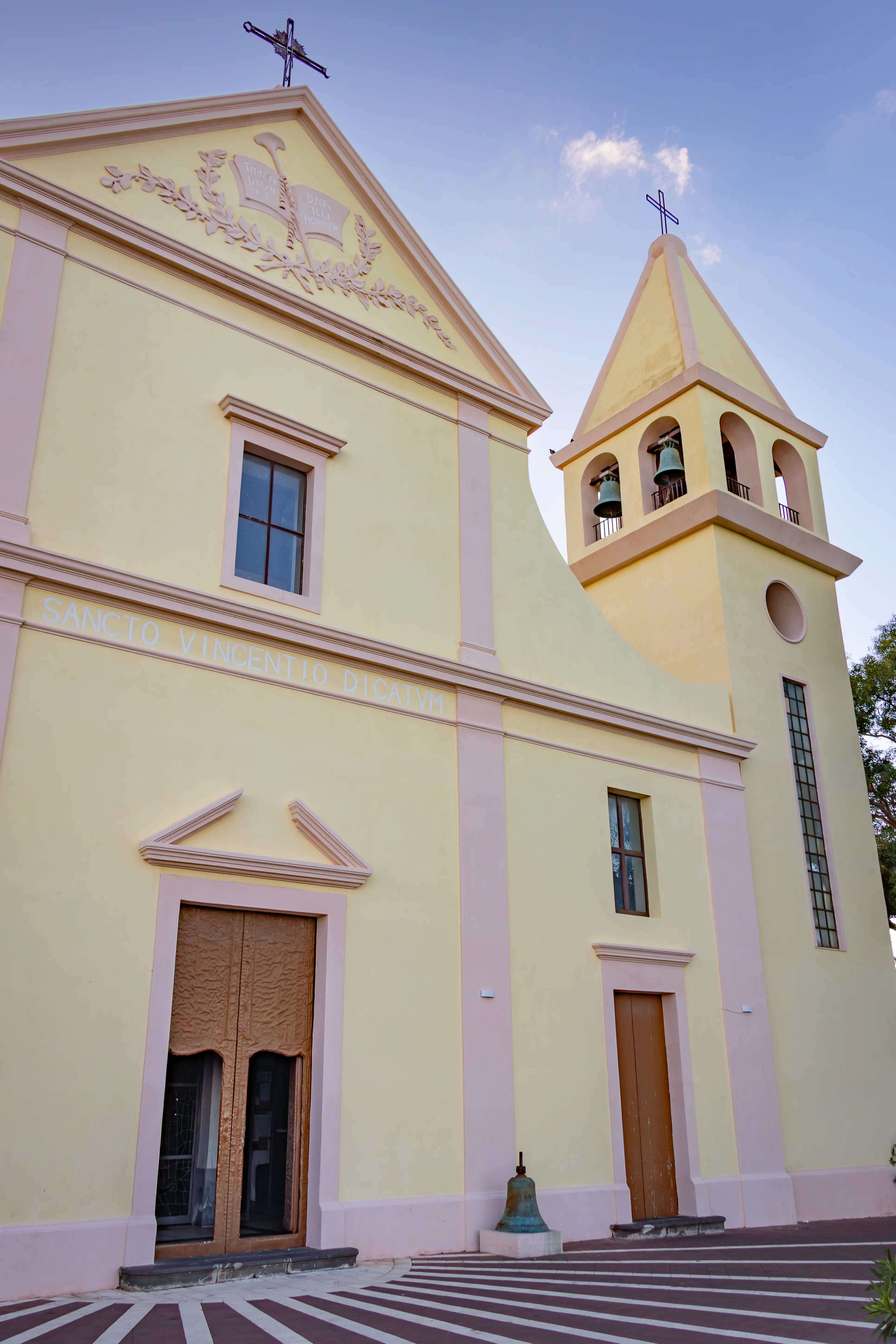 A yellow church façade with a cross on top and a bell tower beside it.