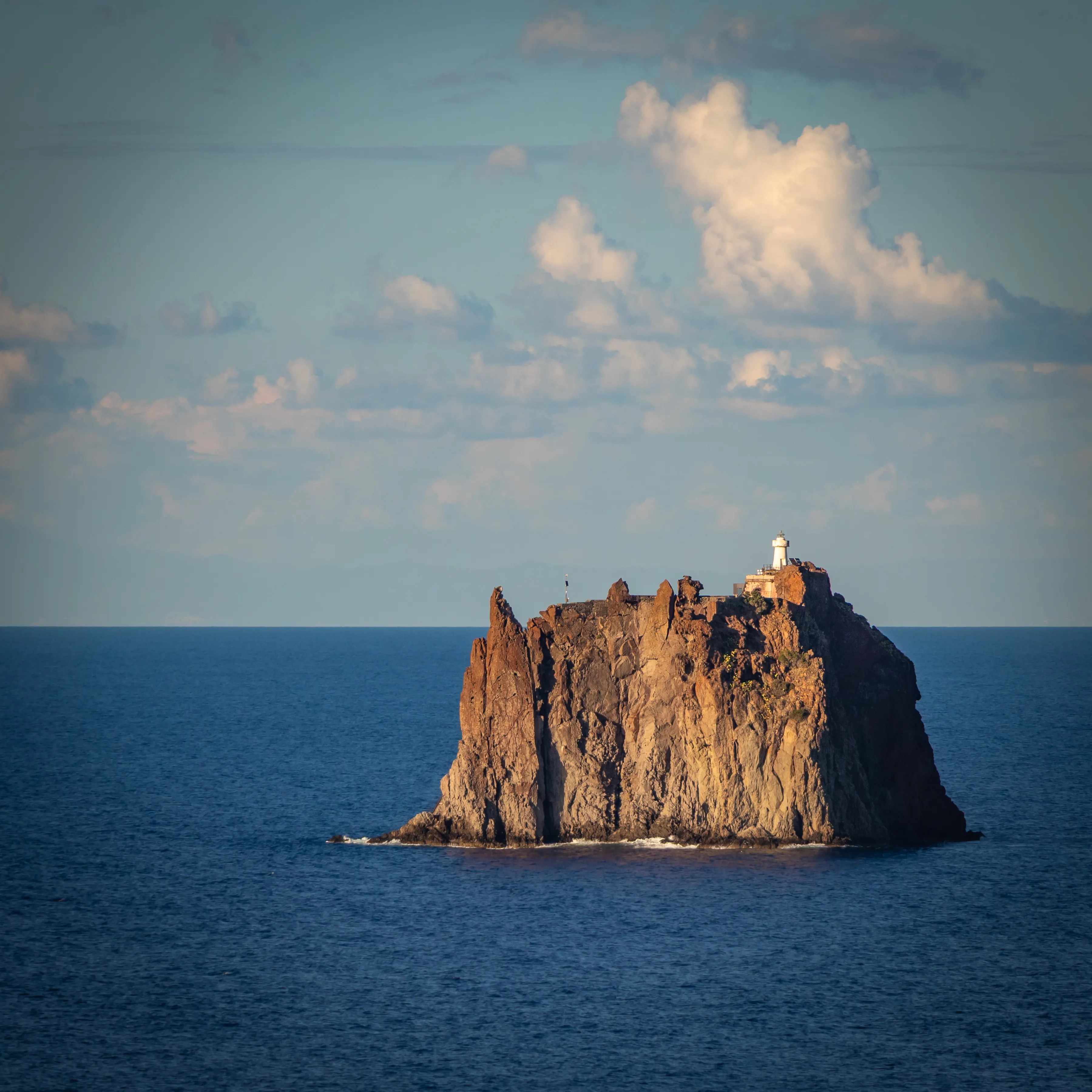 A steep rocky islet in the sea with a small white lighthouse on top.