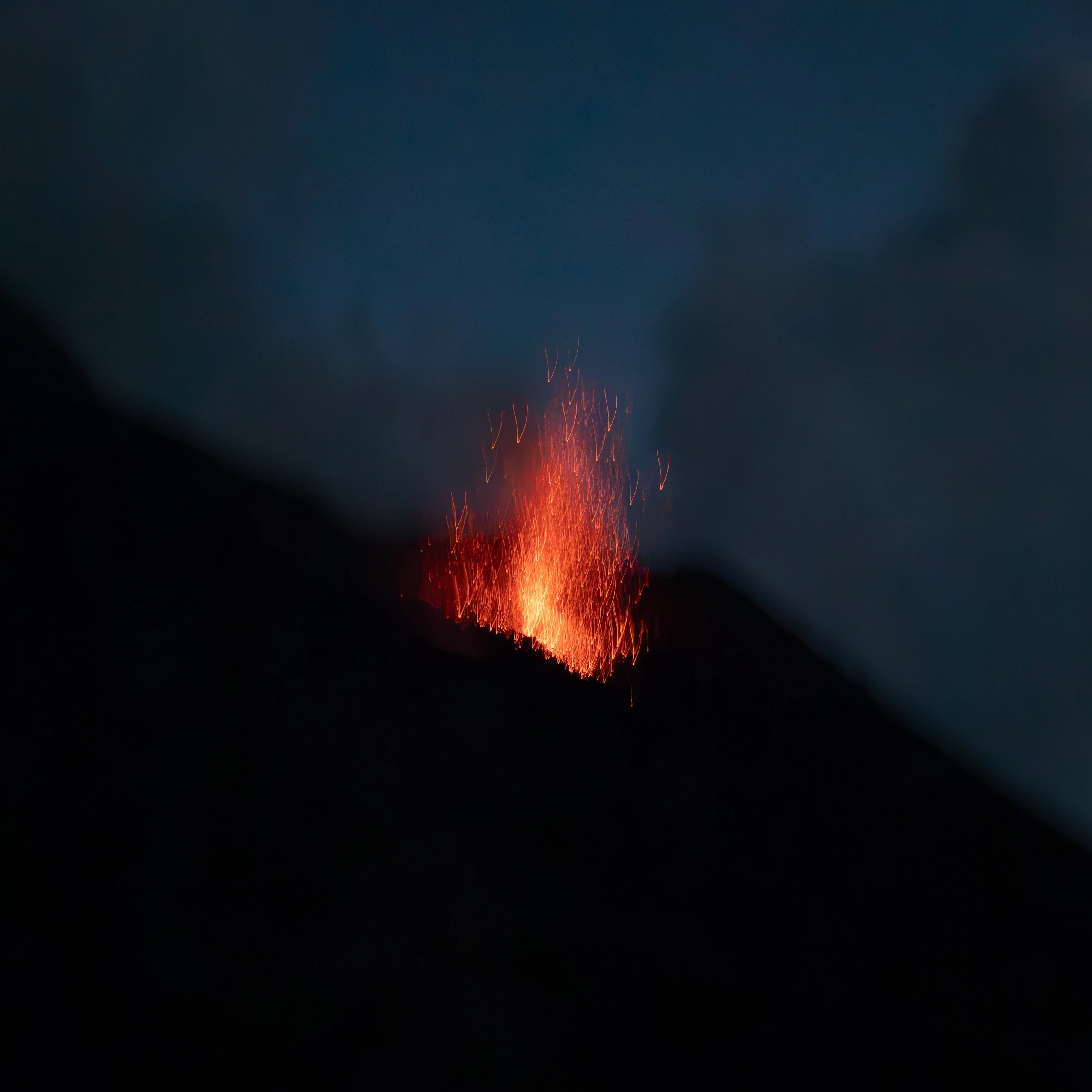 A burst of glowing lava shooting upward from a dark volcanic slope at night.