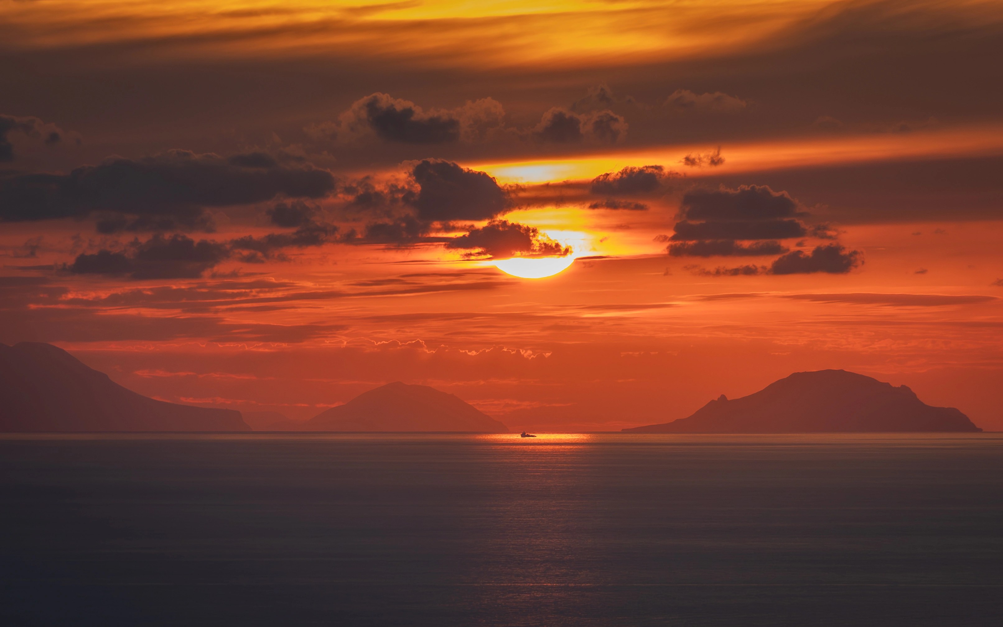The sun setting over the sea with silhouetted islands and orange clouds across the sky.