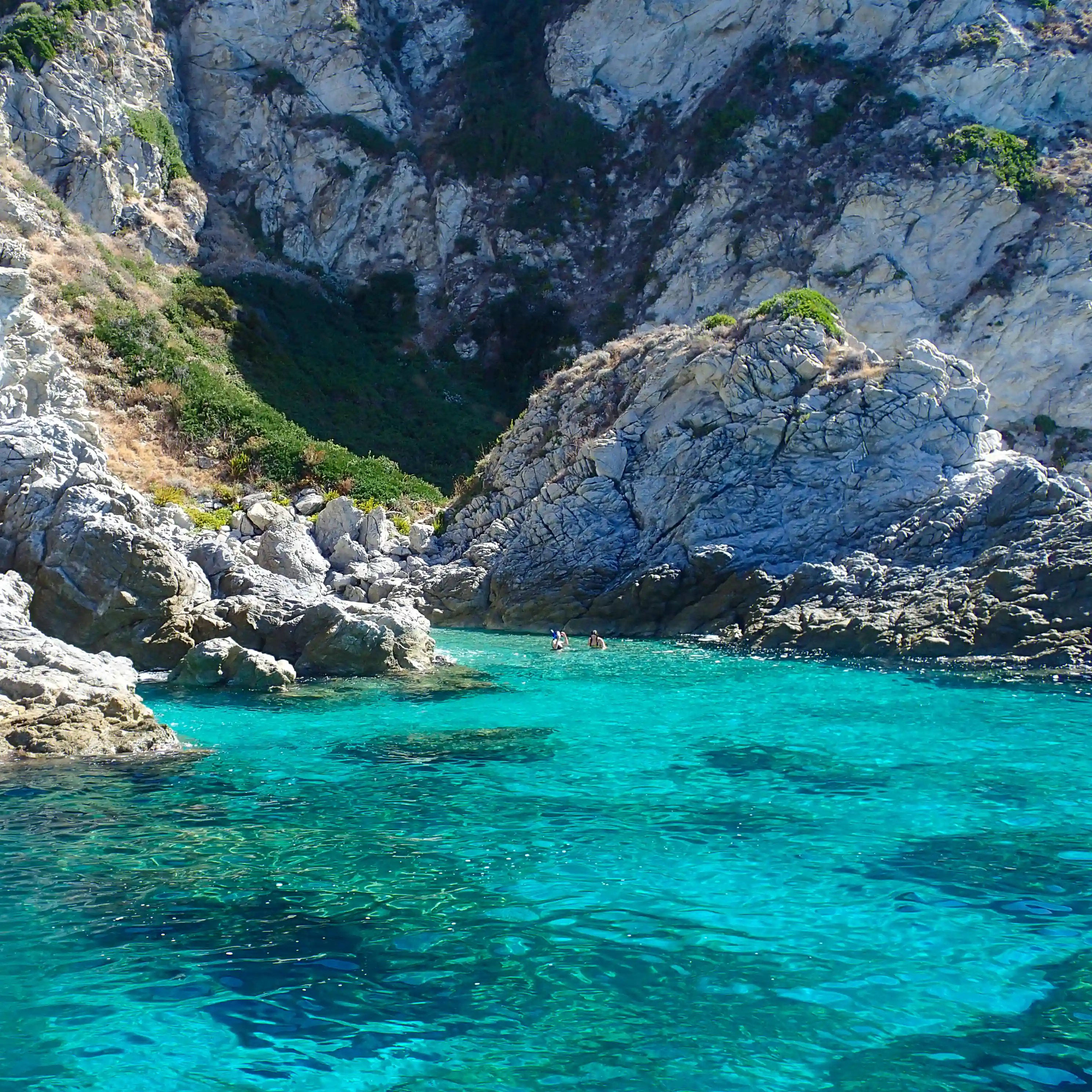 Two people swimming in bright turquoise water surrounded by rocky cliffs.