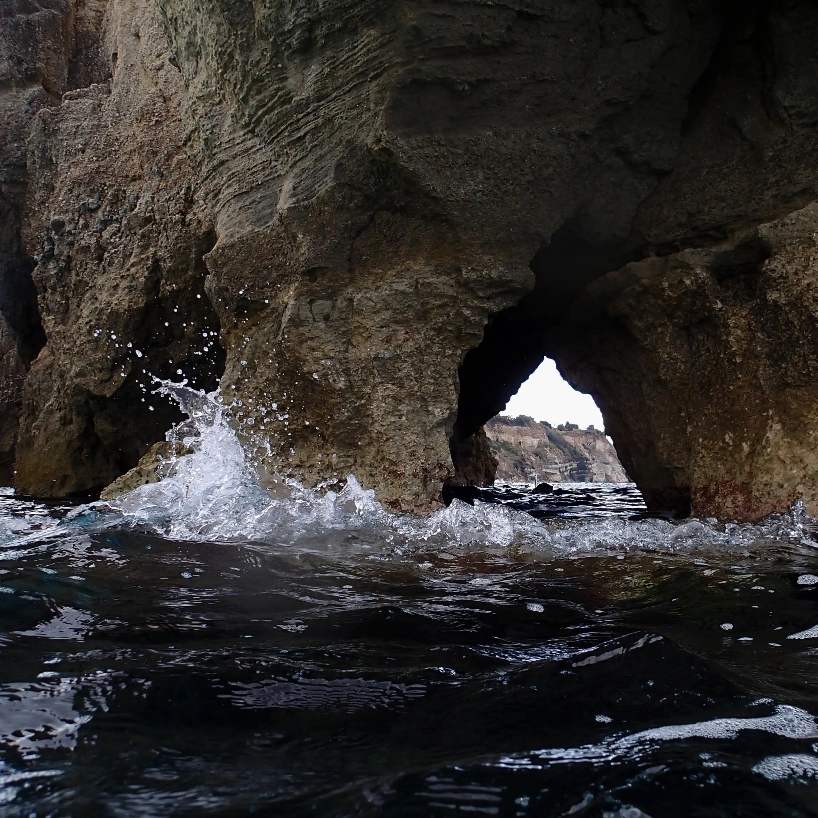 Waves splashing against a rock formation with a natural opening near the waterline.
