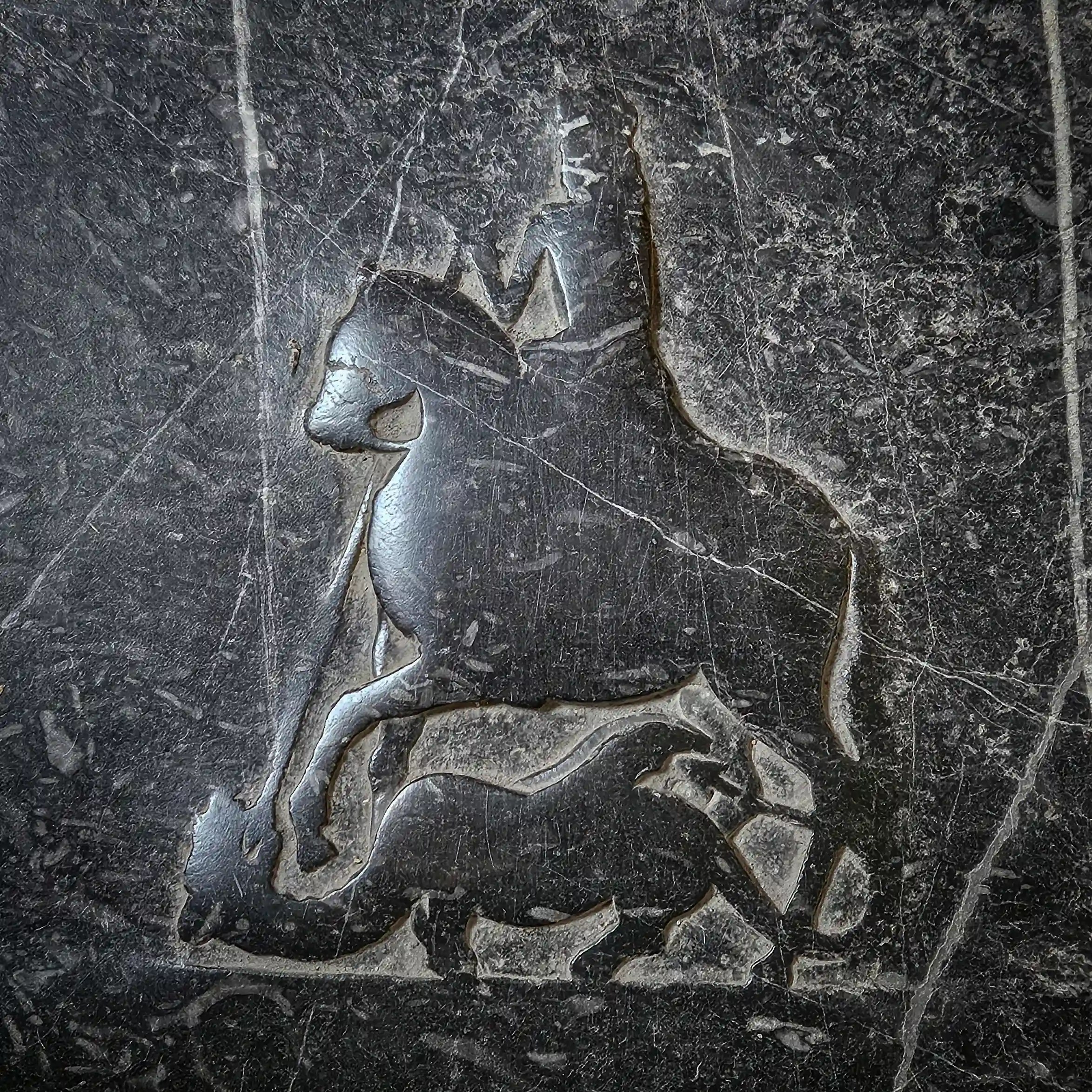 A dark stone relief shows a rider on a horse above an animal on the ground.