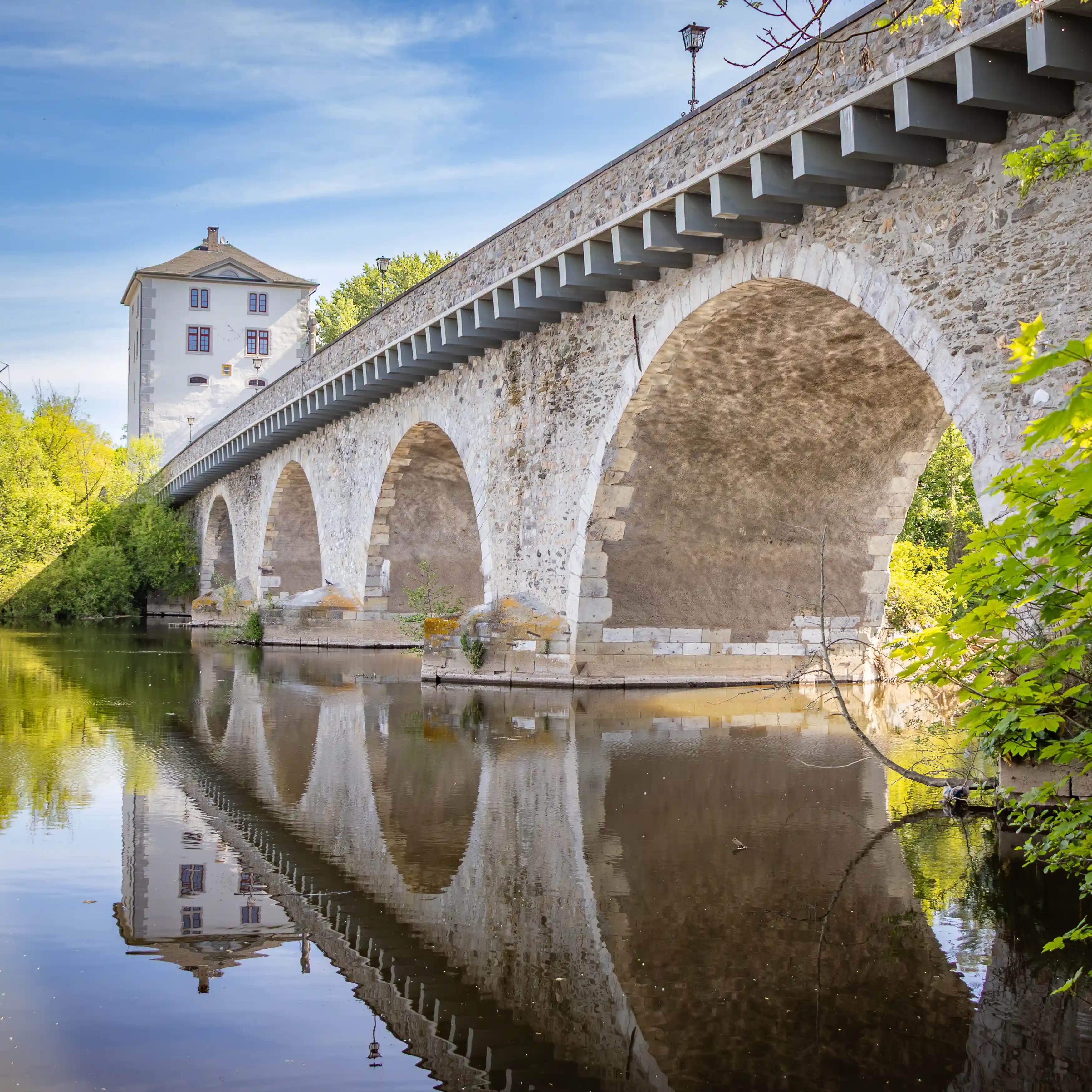 A stone arch bridge crosses the Lahn River with a white tower visible at one end.