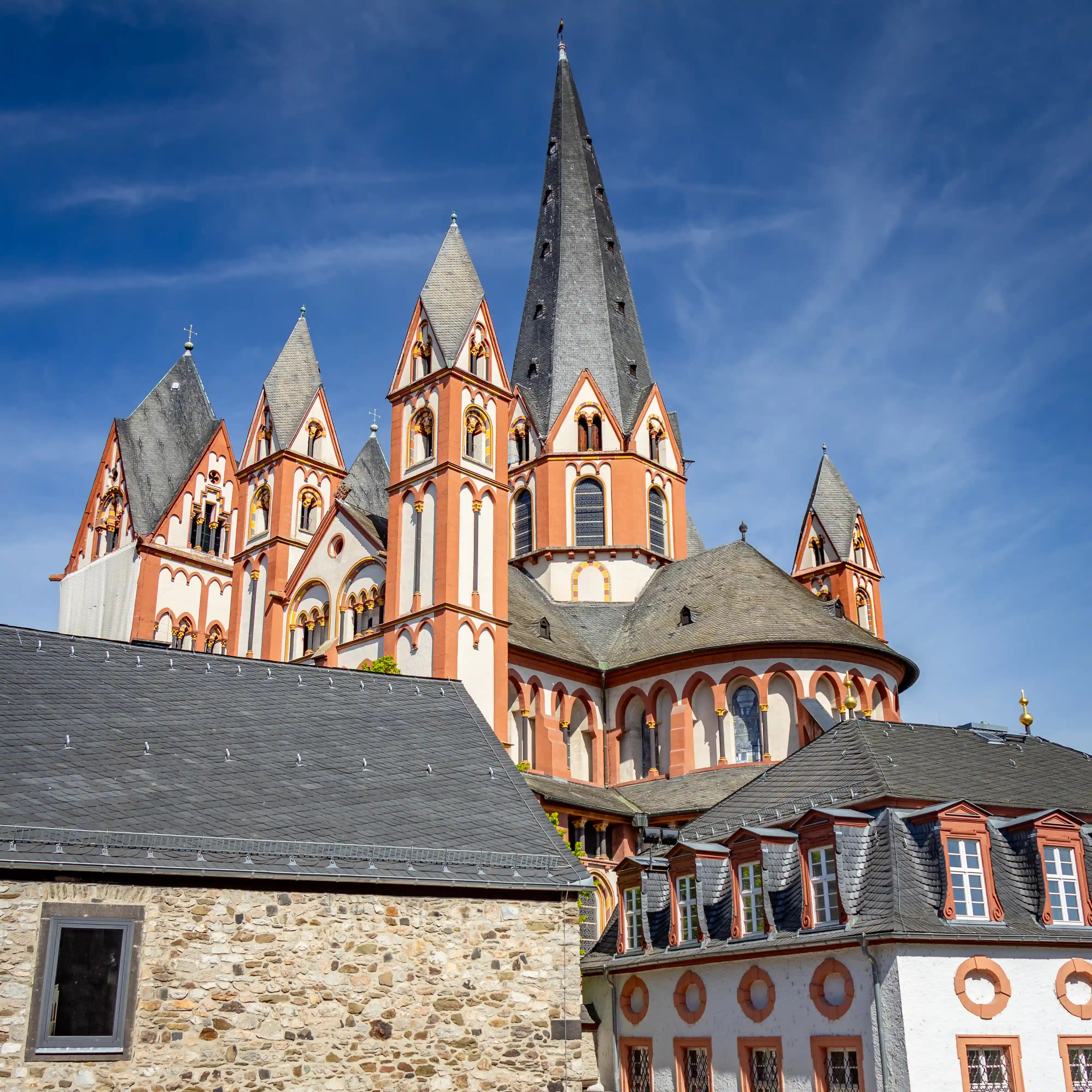 Limburg Cathedral rises behind slate rooftops with several towers visible against a blue sky.