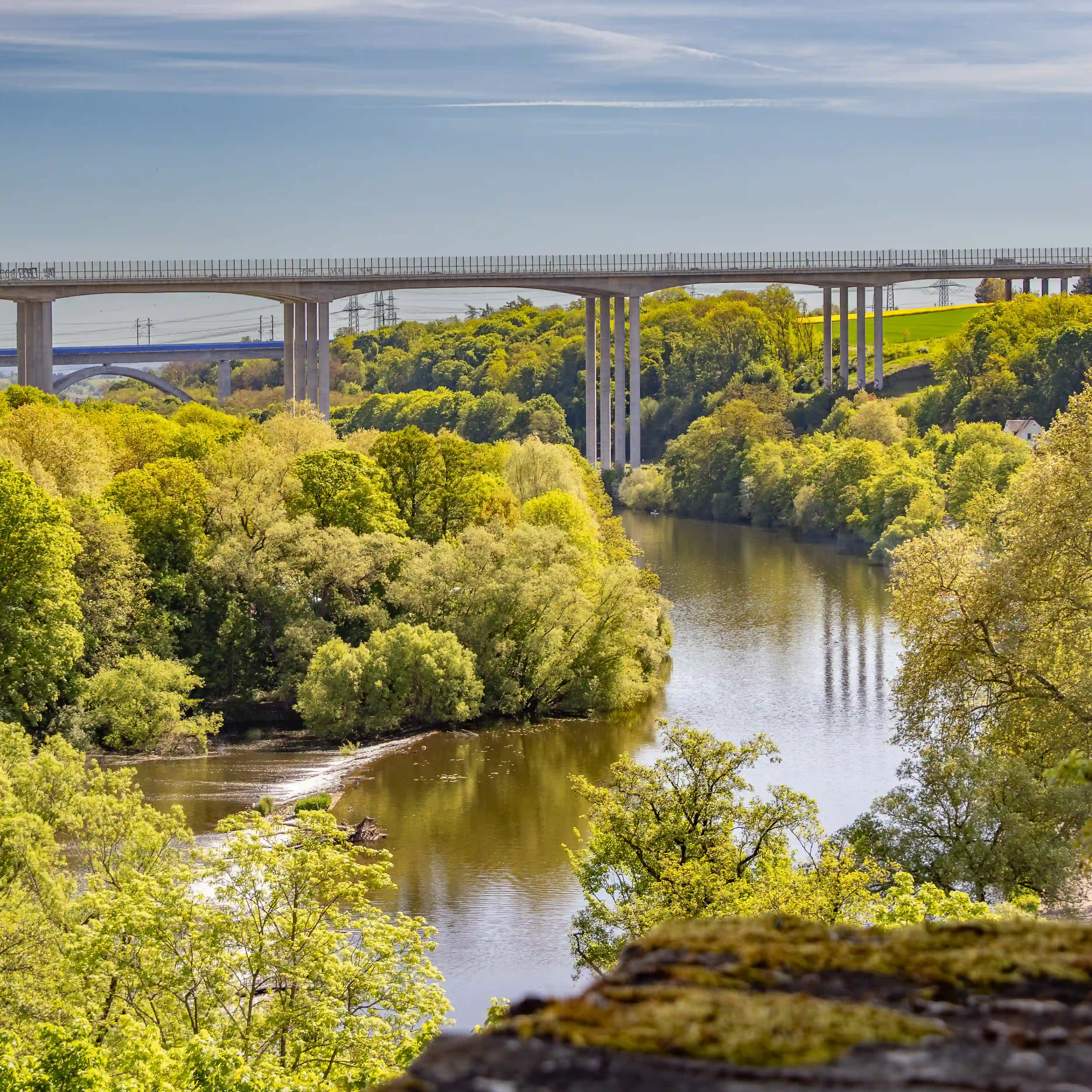 A tall modern bridge crosses the Lahn Valley above trees and a winding river.