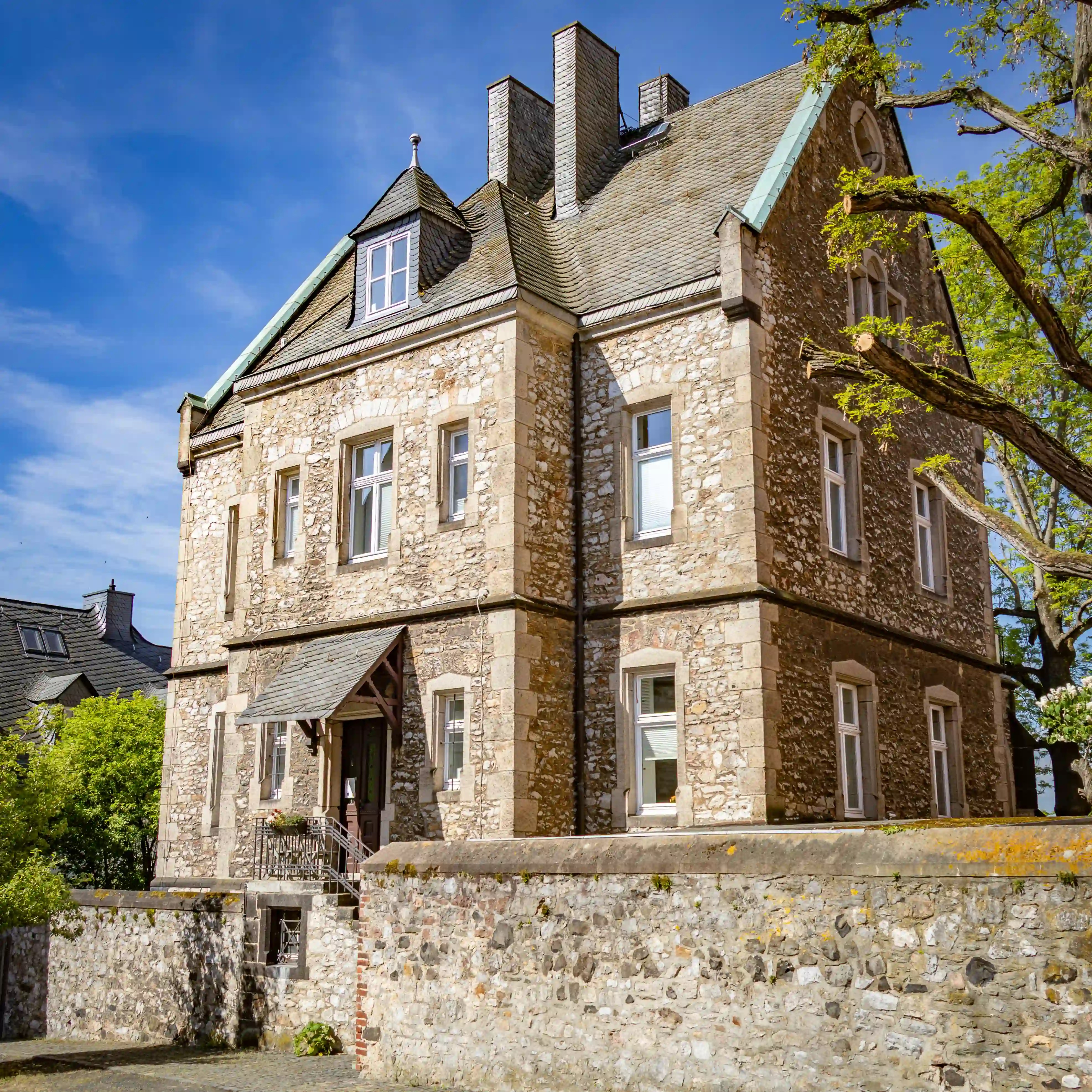 A stone building with a slate roof stands behind a low stone wall under a blue sky.
