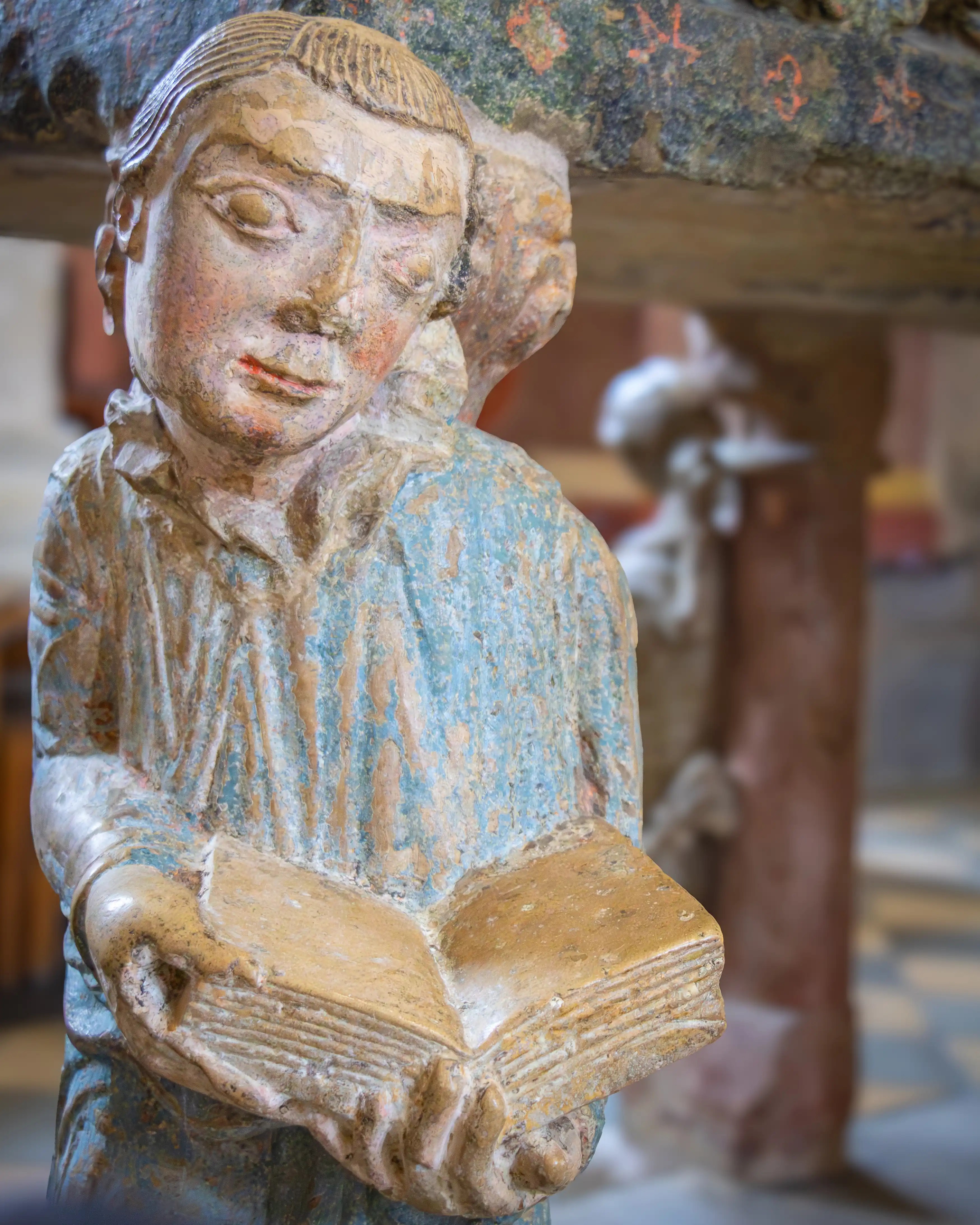 A carved figure holds an open book on the side of a painted stone tomb.