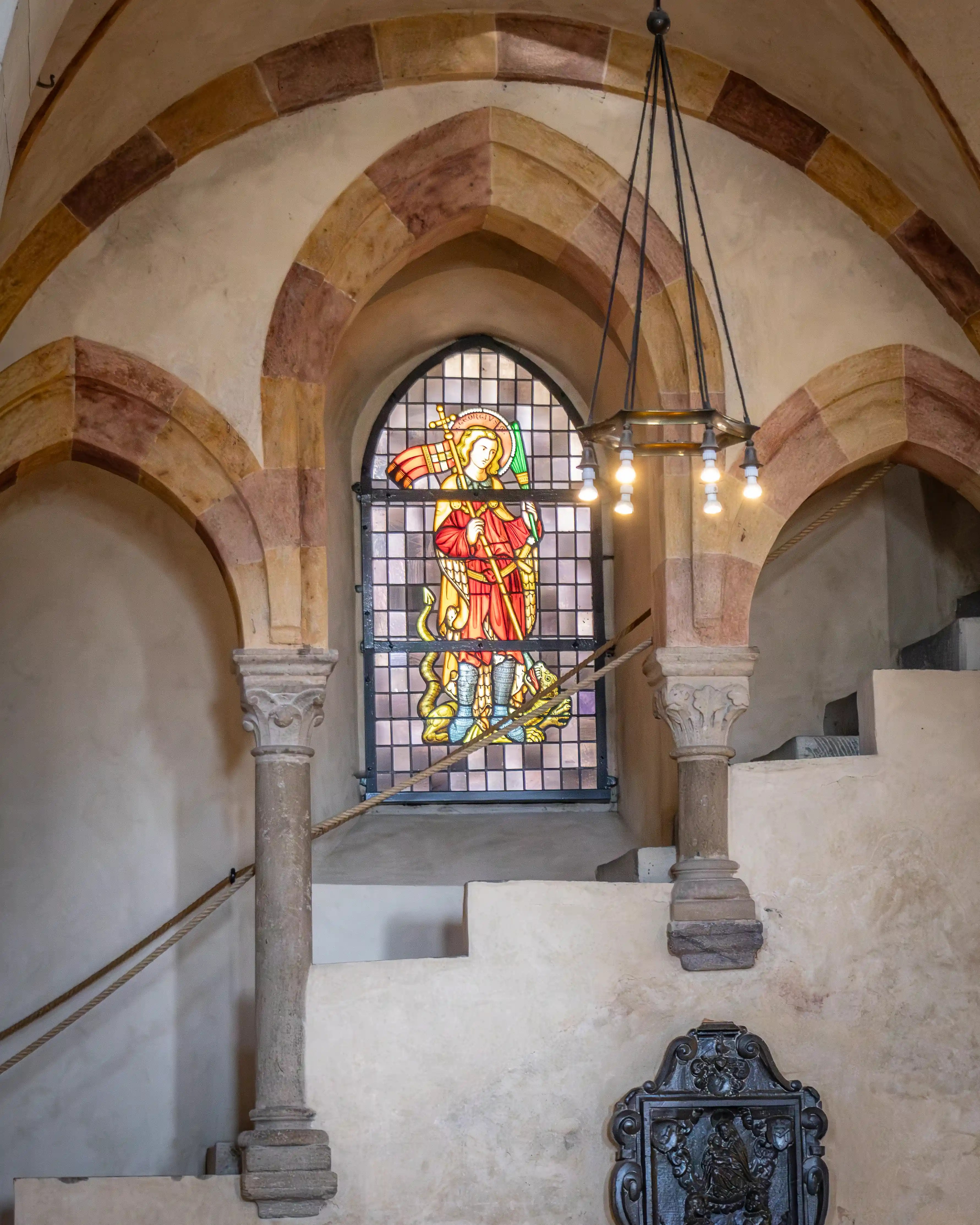 A stained-glass window stands behind stone arches and columns inside a church.