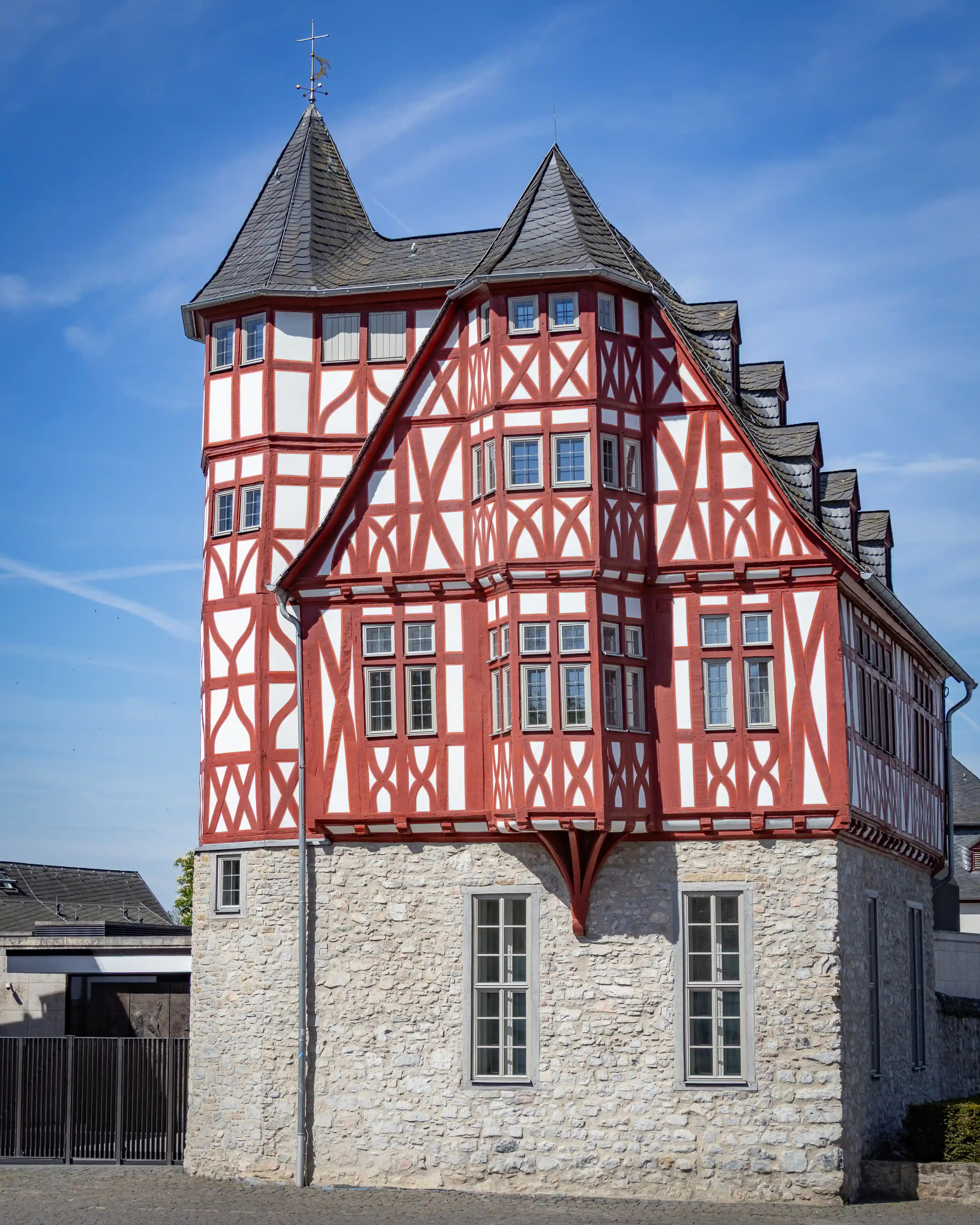 A red-and-white half-timbered building rises above a stone lower floor under a blue sky.