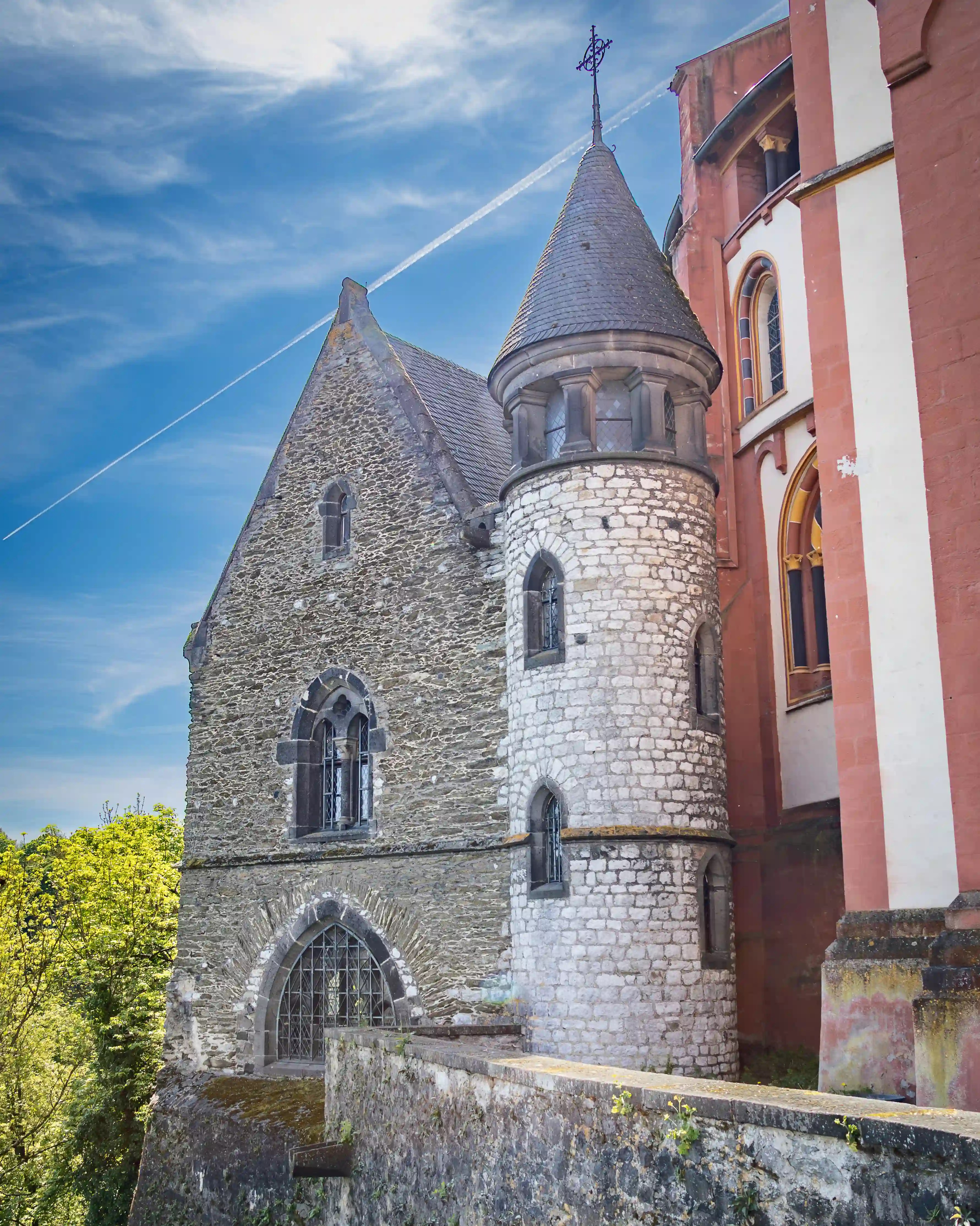 A round stone tower and older stone building stand beside the red-and-white cathedral wall.
