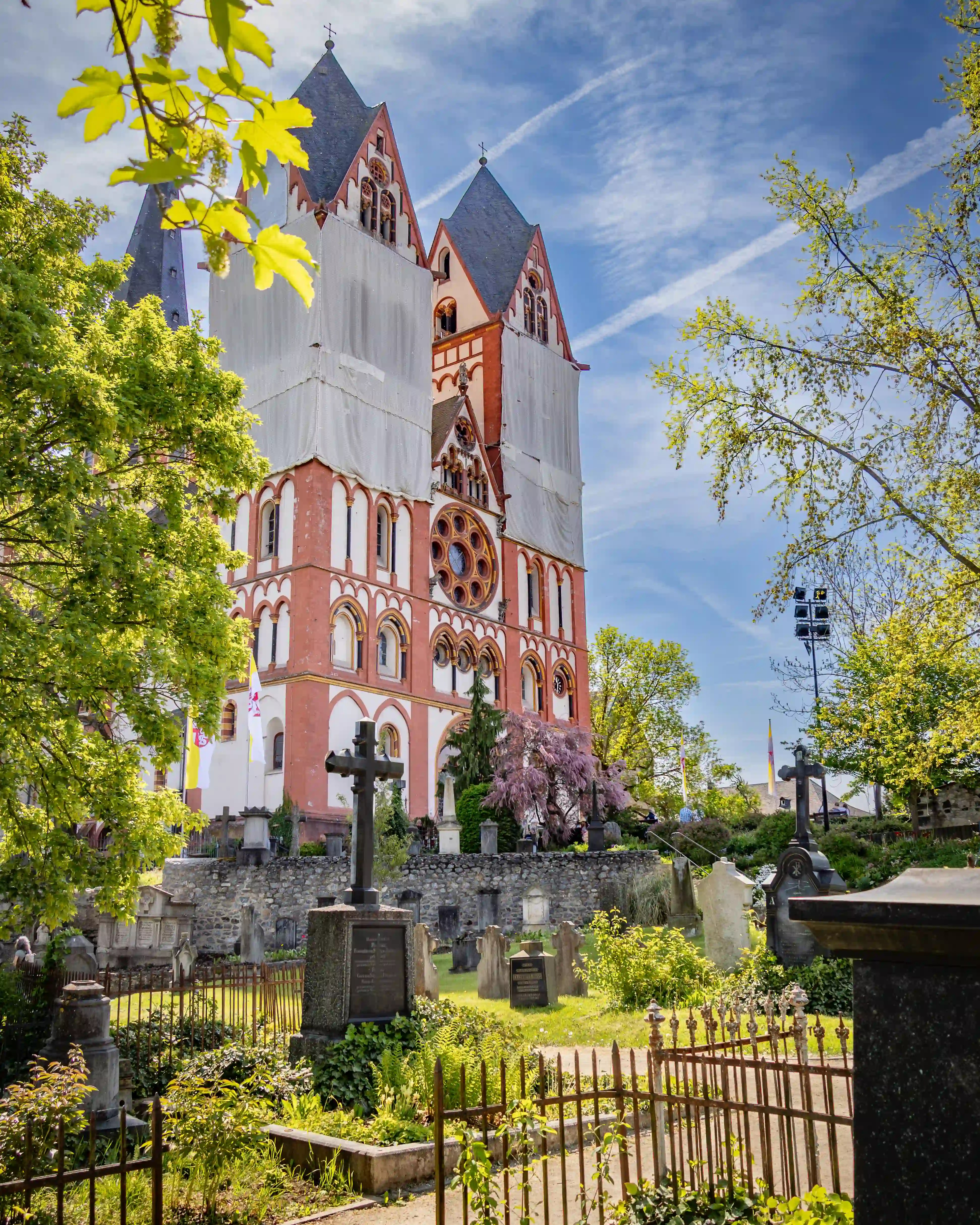 Limburg Cathedral rises behind a cemetery with gravestones, trees, and spring flowers.