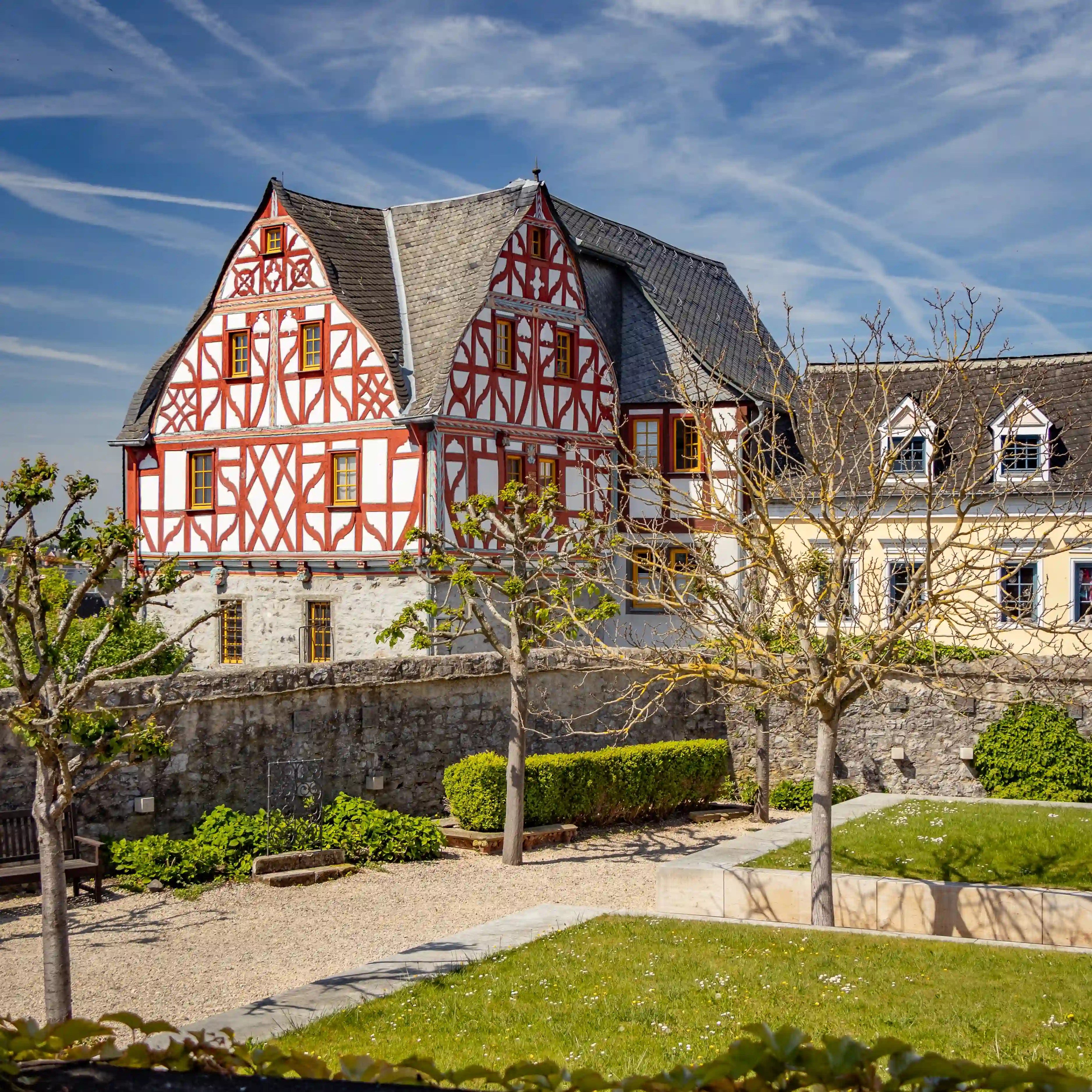 A red-and-white half-timbered building stands behind a garden and low stone wall.