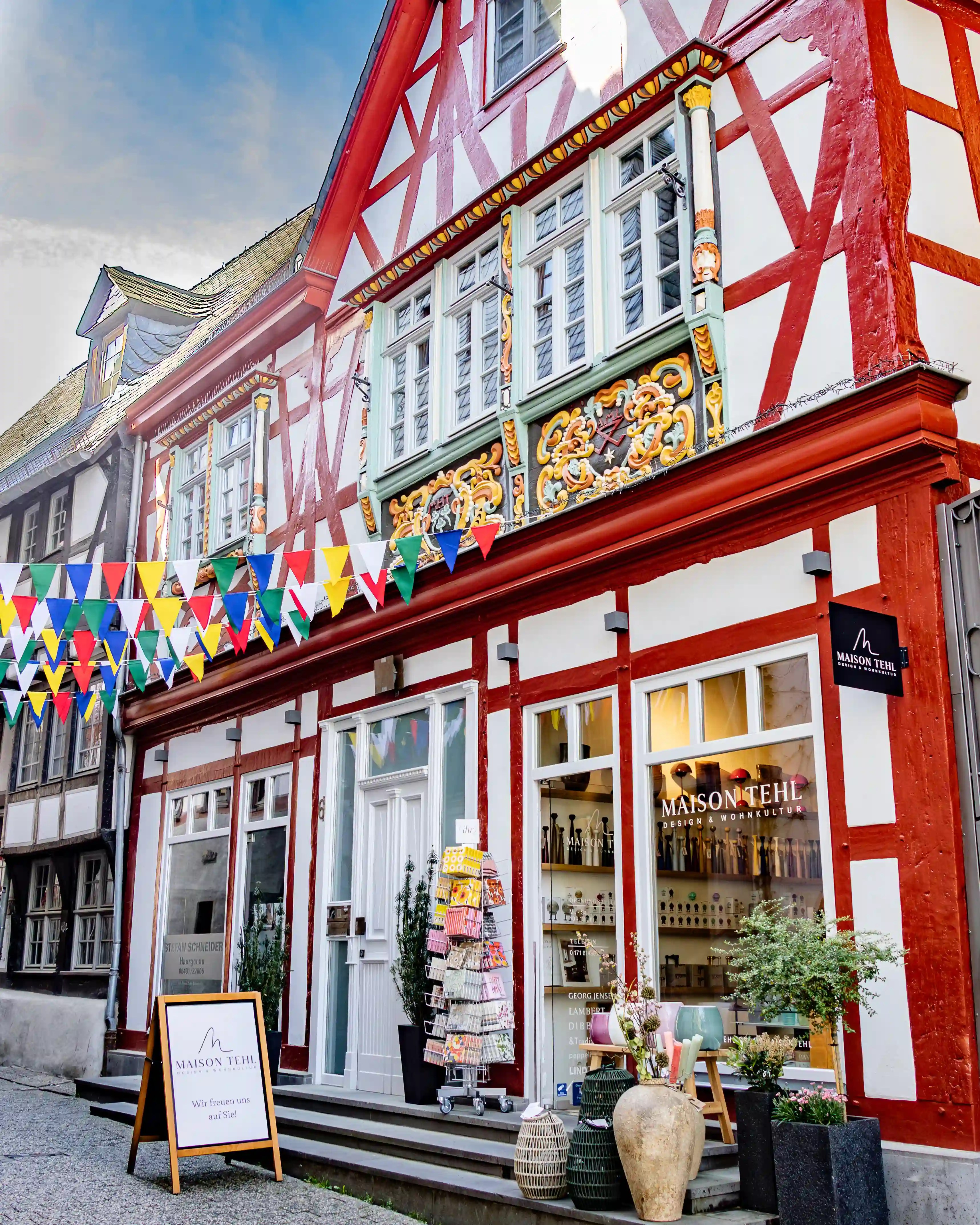 A red-and-white half-timbered building has carved trim, large windows, and colorful flags.