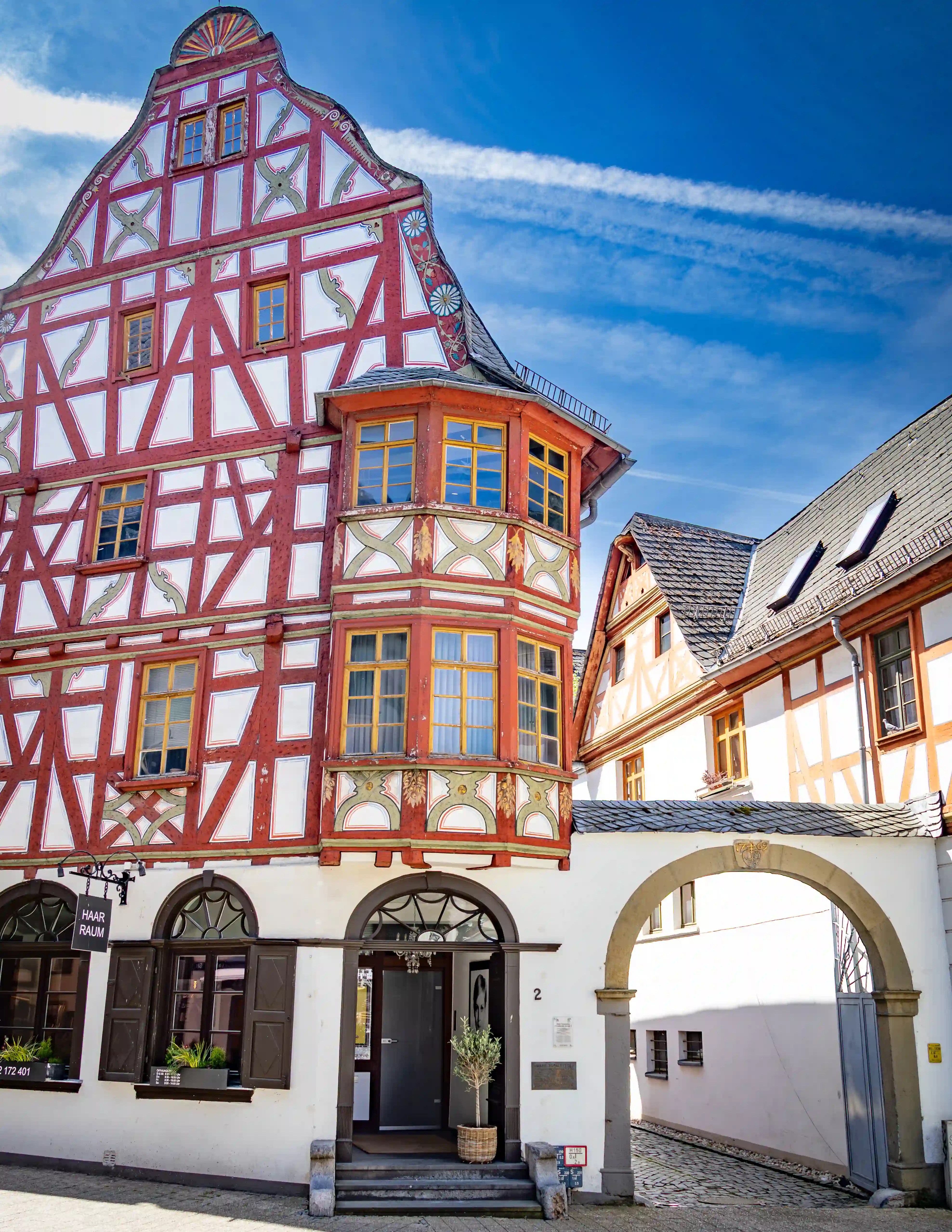 A red half-timbered building with an oriel window stands beside an arched passageway.