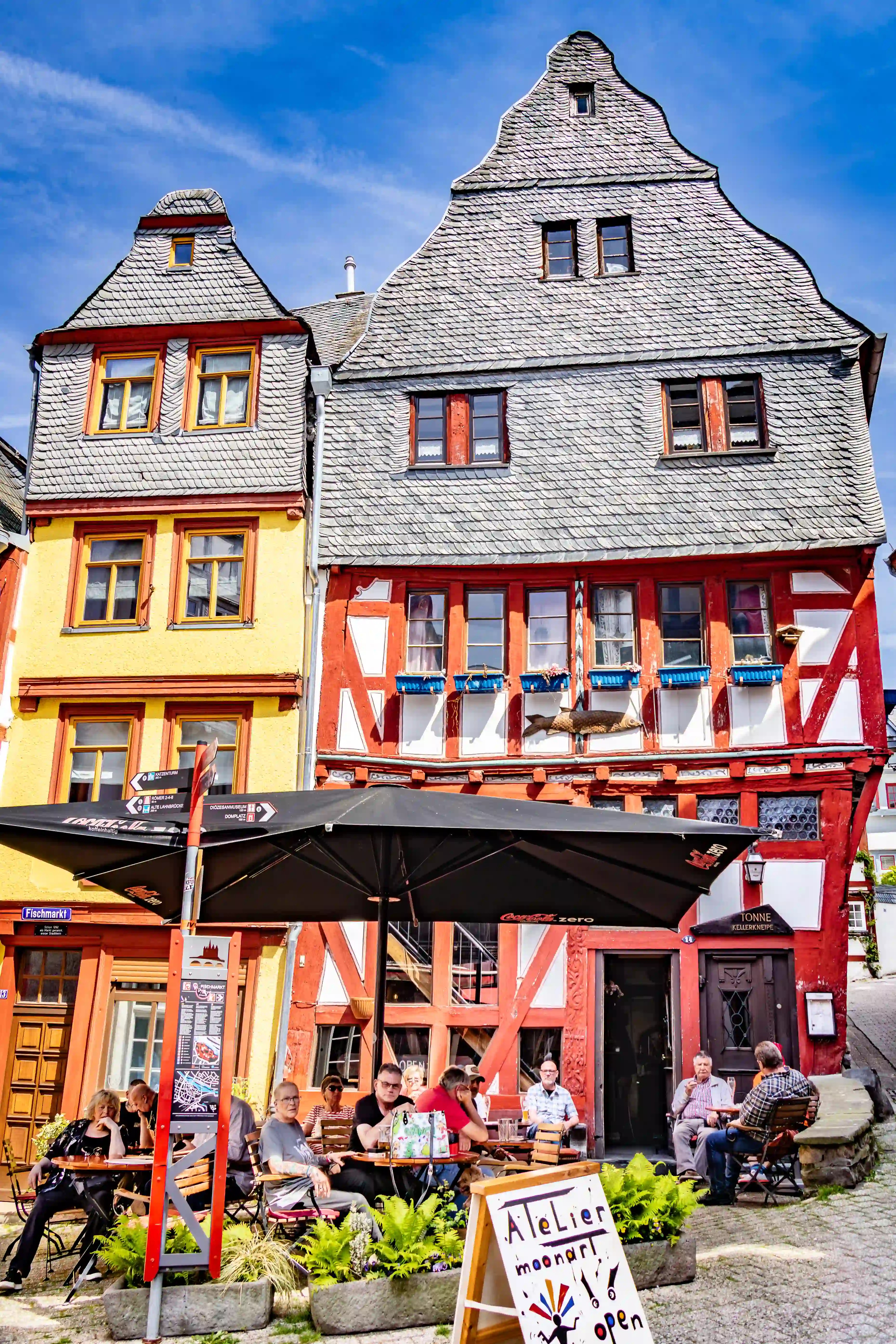 A yellow house and a red half-timbered building stand above outdoor cafe tables.