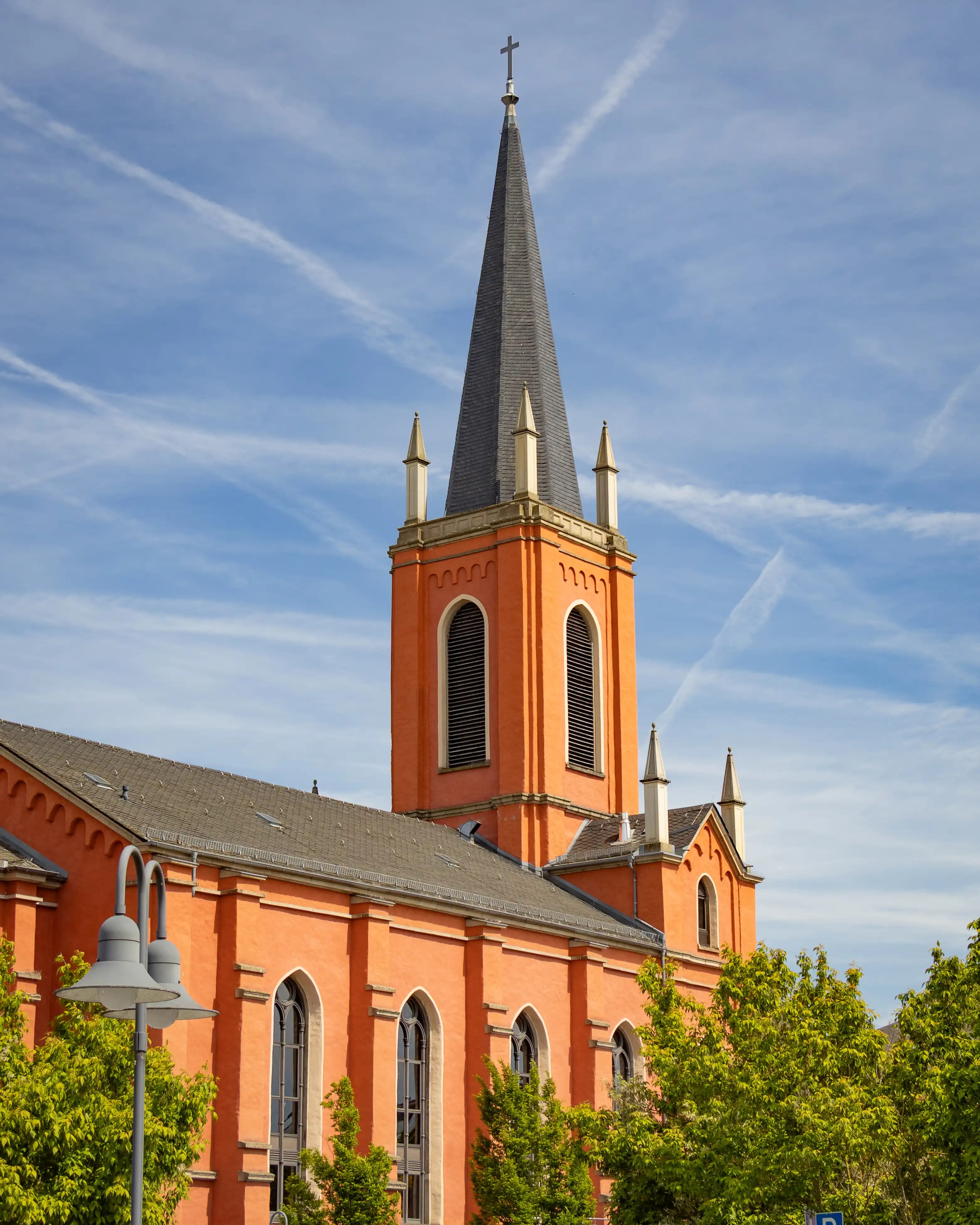 An orange church tower with a dark spire rises above trees beneath a blue sky.