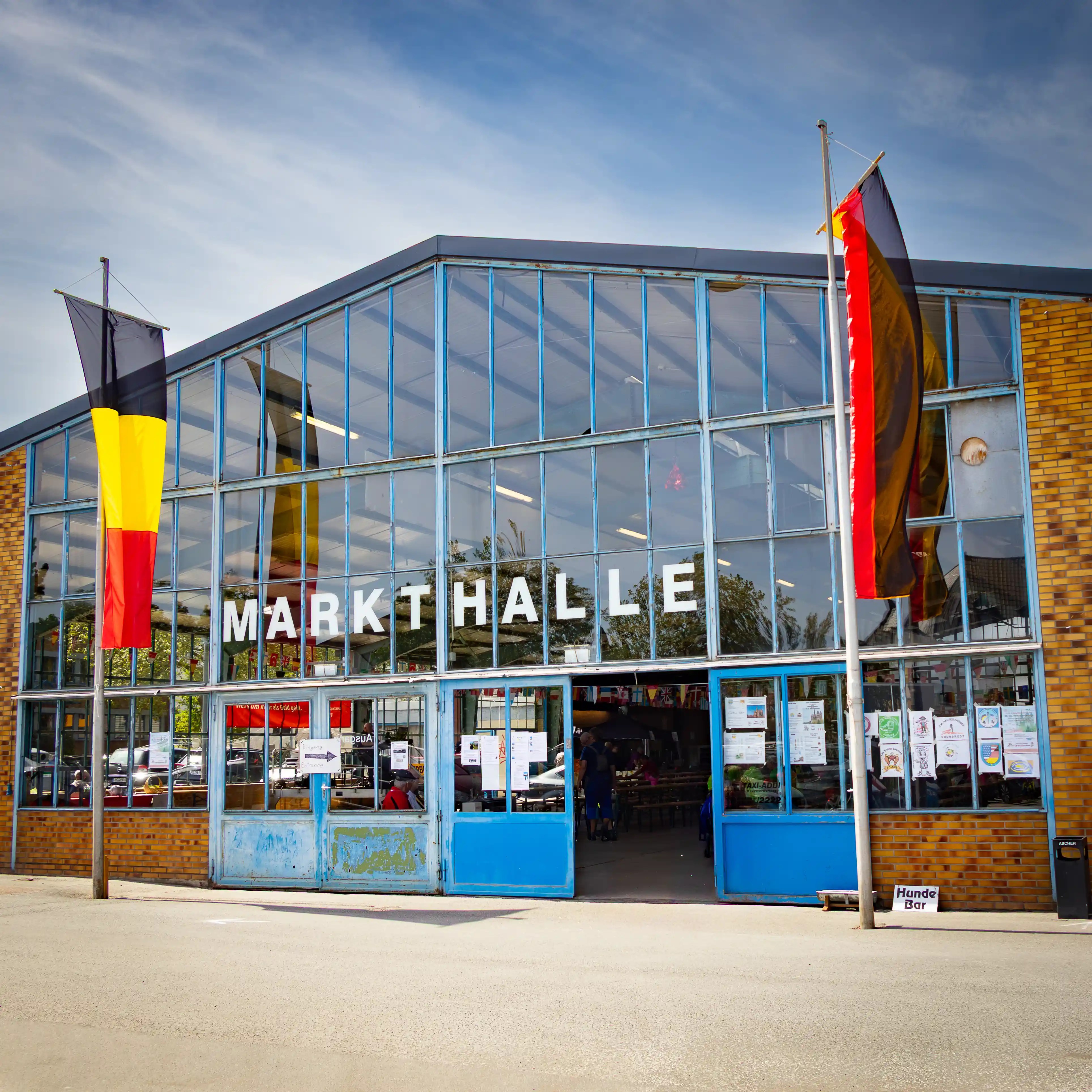 German flags stand outside a glass-fronted building labeled Markthalle.