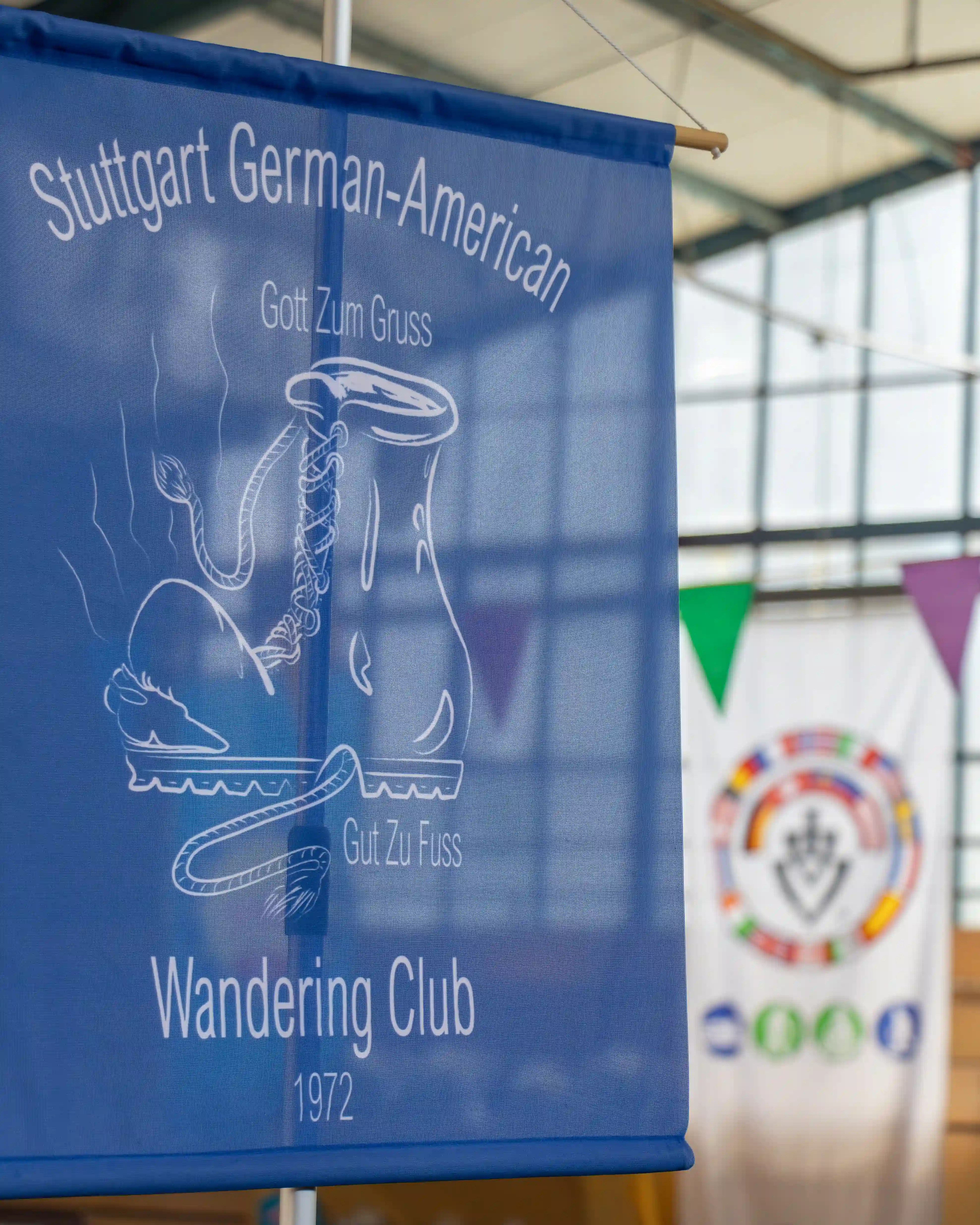 A blue Stuttgart German-American Wandering Club banner hangs inside a hall with flags behind it.