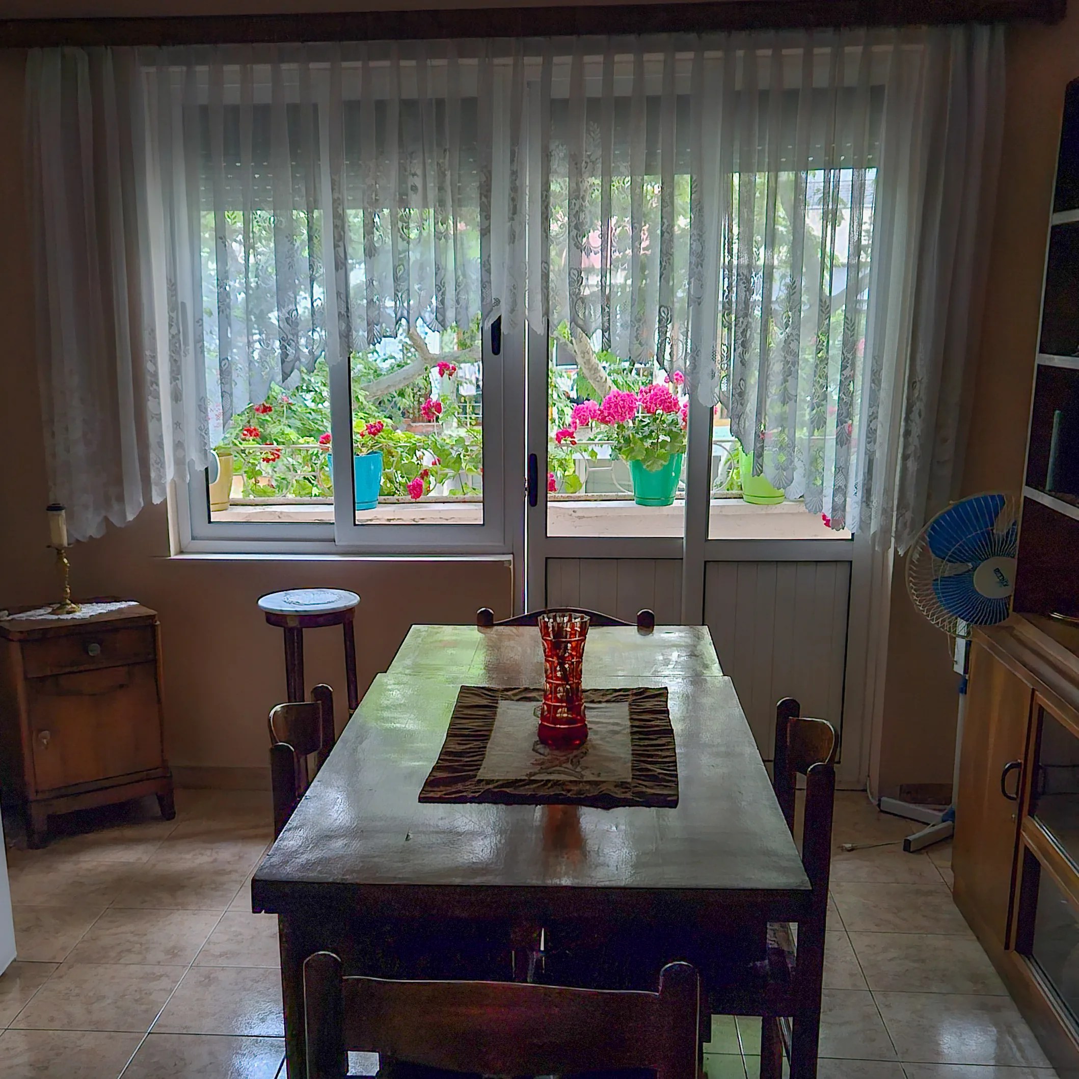 Dining area with a wooden table and large window overlooking flowers outside.