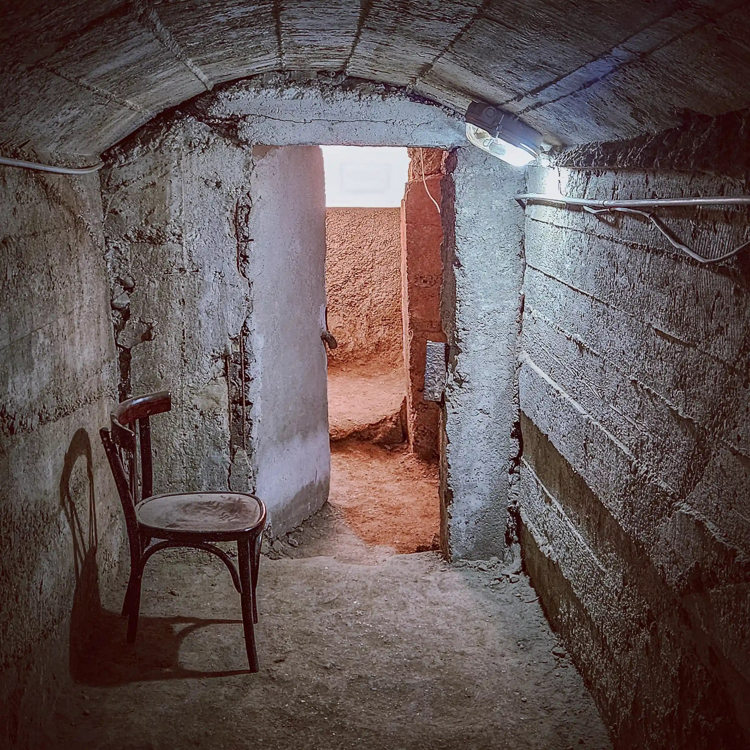 Narrow concrete corridor with a single chair inside the bunker at the House of Leaves museum in Tirana, Albania.
