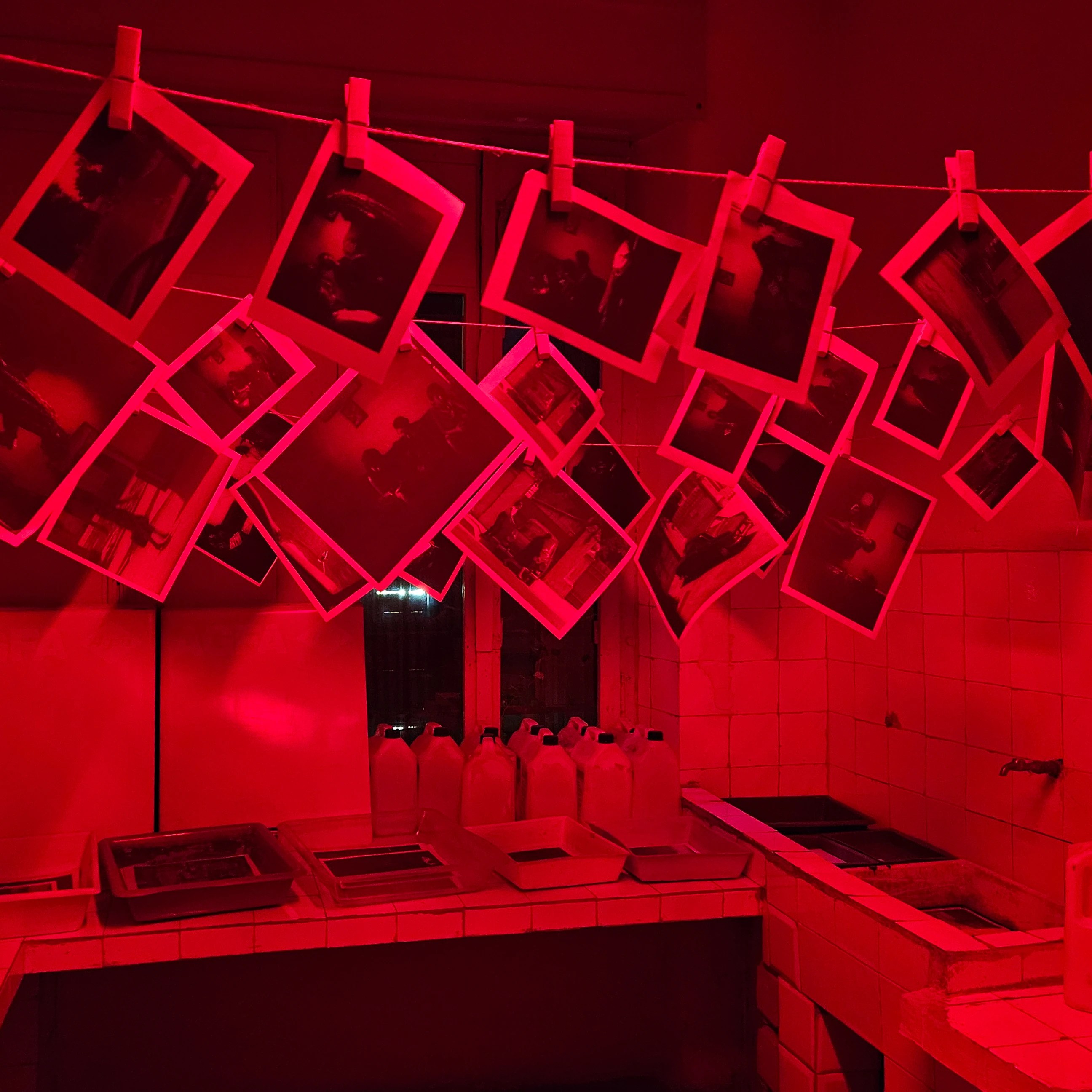 Photographs hanging in a red-lit darkroom exhibit at the House of Leaves museum in Tirana.