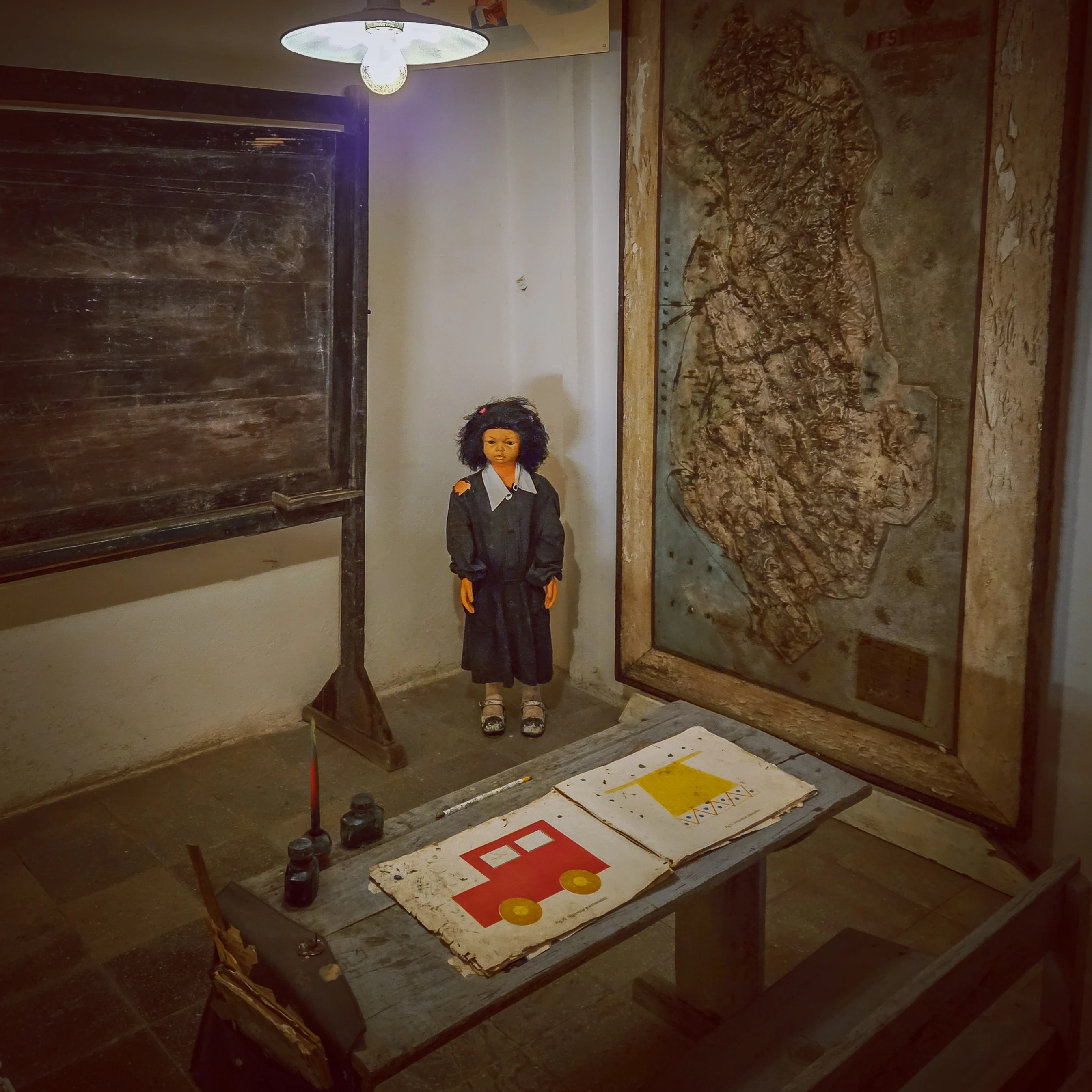 Classroom exhibit with a school desk, chalkboard, doll, and relief map of Albania inside Bunk'Art 1.