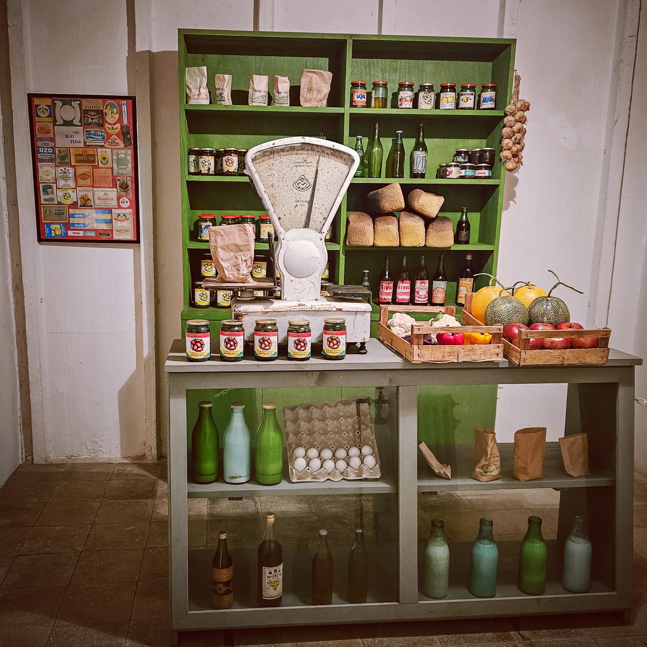 Recreated communist-era grocery store display with food products, produce, and a large scale inside Bunk'Art 1.