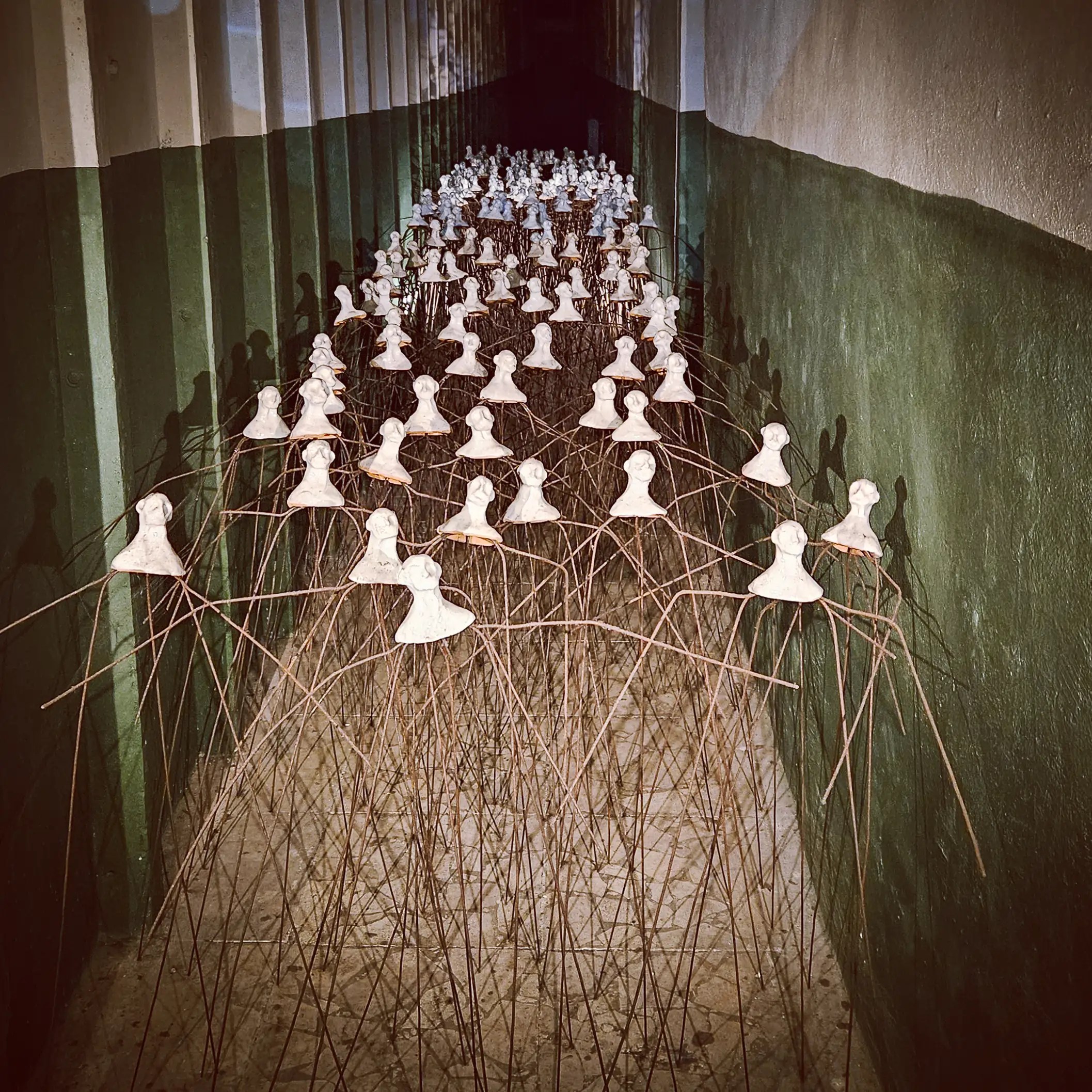 Art installation of dozens of white busts connected by thin metal rods in a corridor at Bunk'Art 1.