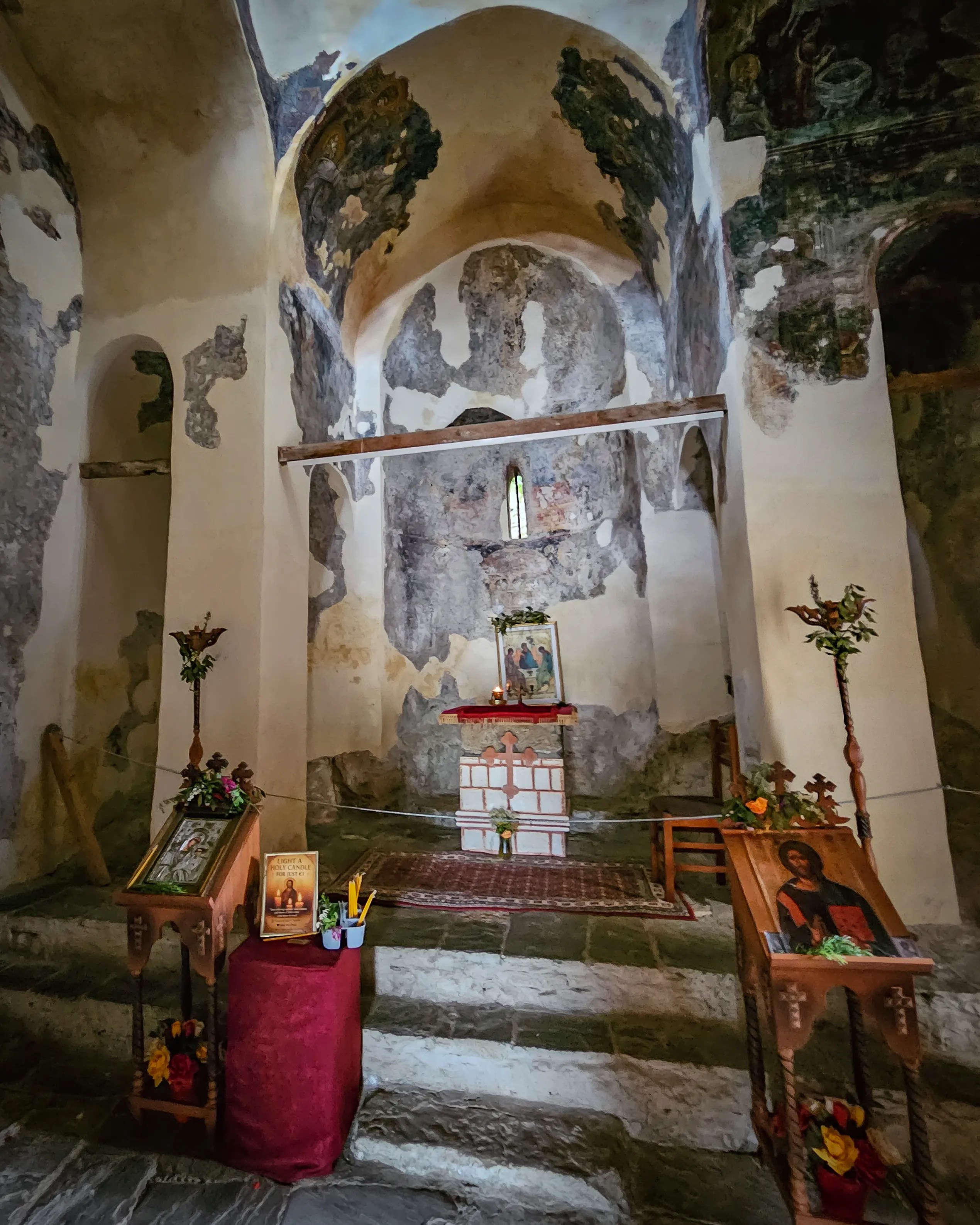 Interior of Holy Trinity Church in Berat Castle with a small altar, worn frescoes, and stone steps leading to the apse.