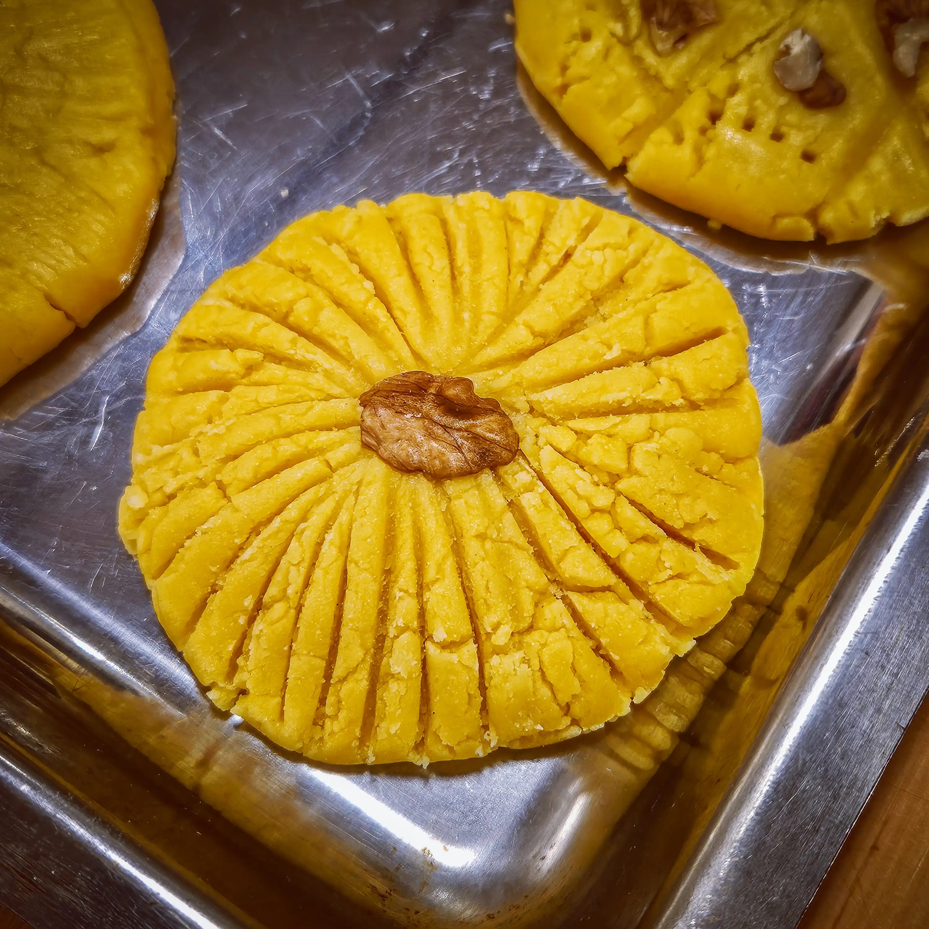 Unbaked Albanian butter cookies decorated with a walnut and arranged on a metal tray during a cooking class in Tirana.