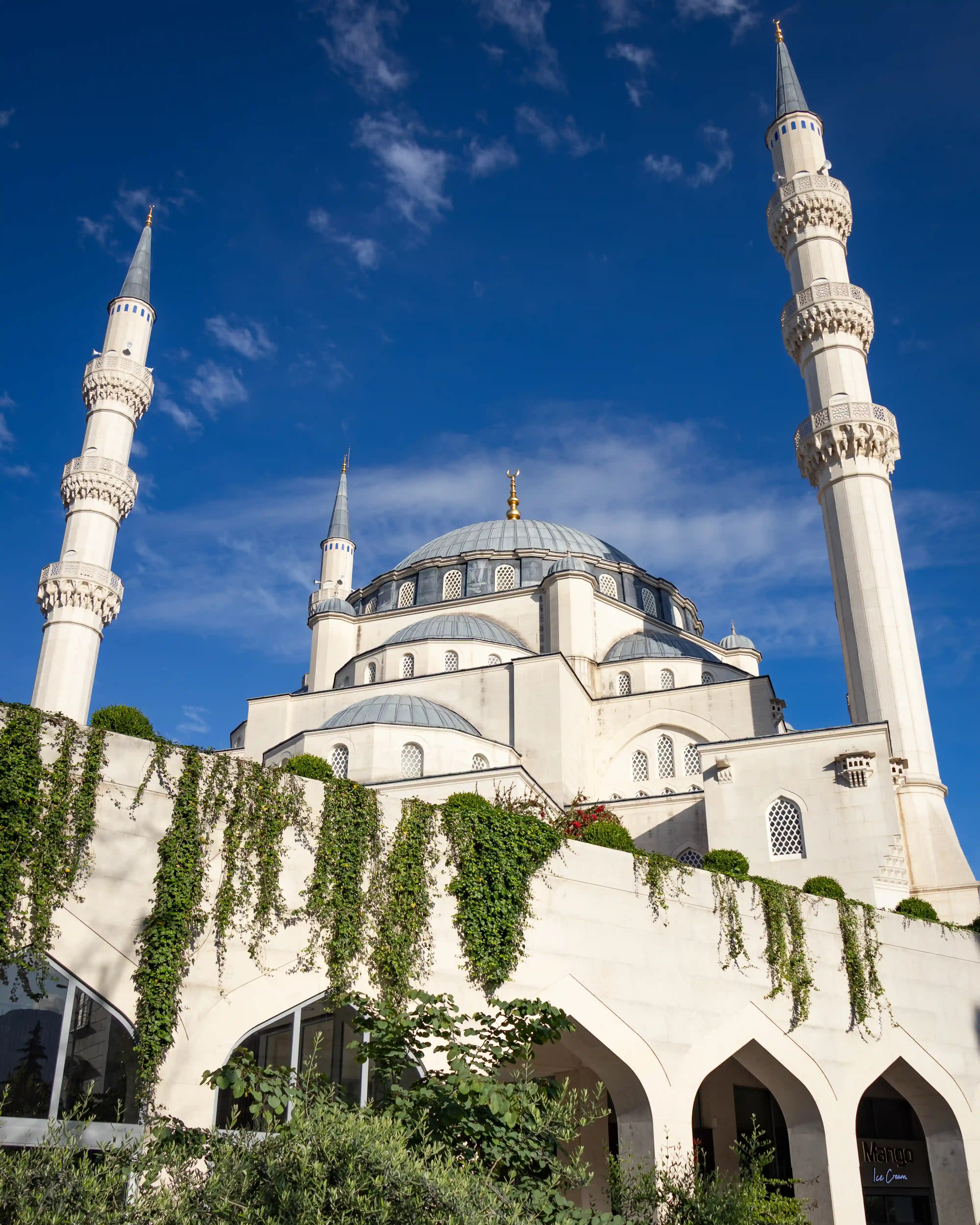 The Grand Mosque of Tirana with its large dome and four minarets against a blue sky.