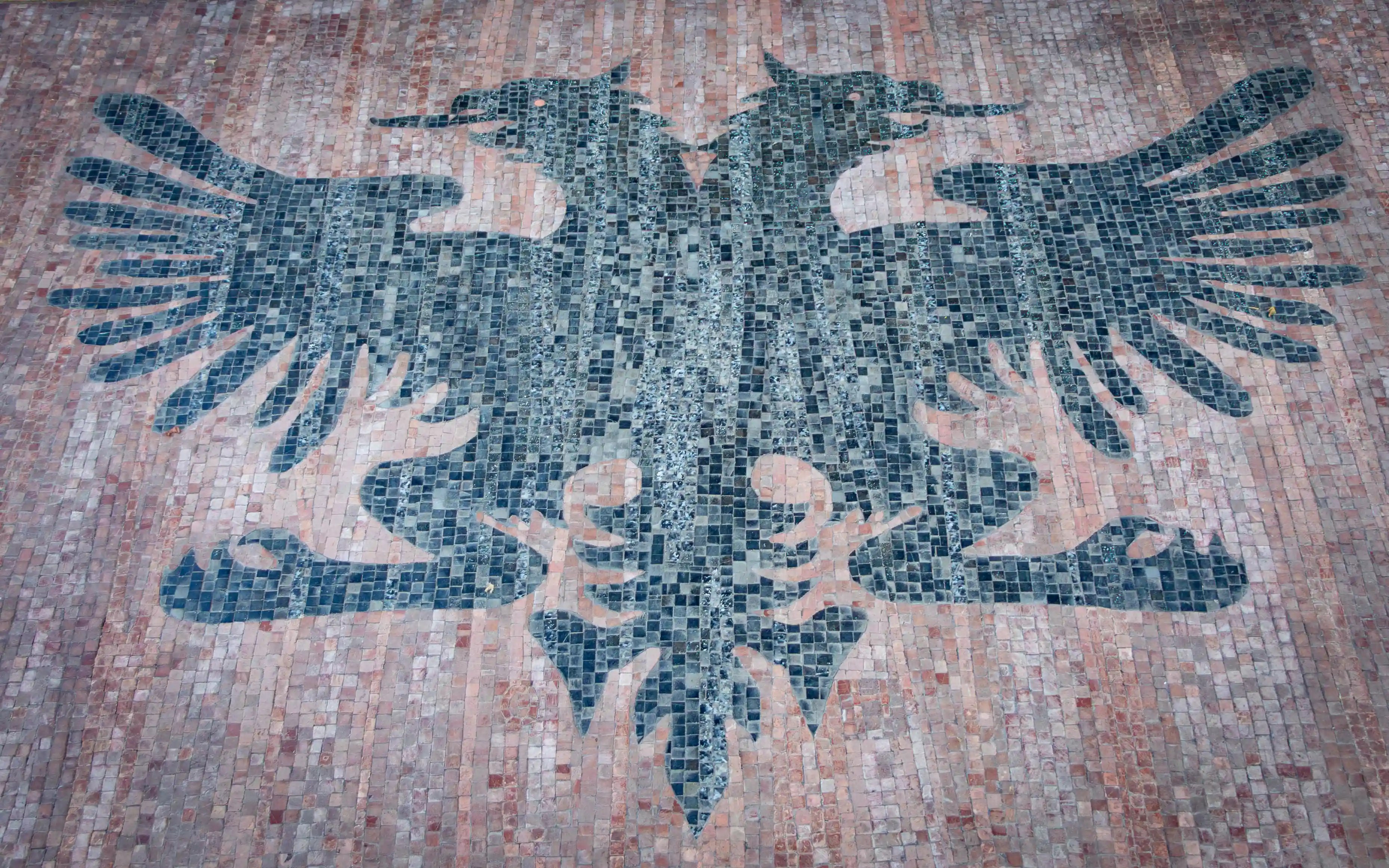 A black double-headed eagle mosaic set into a brick-paved surface, representing the national symbol of Albania.