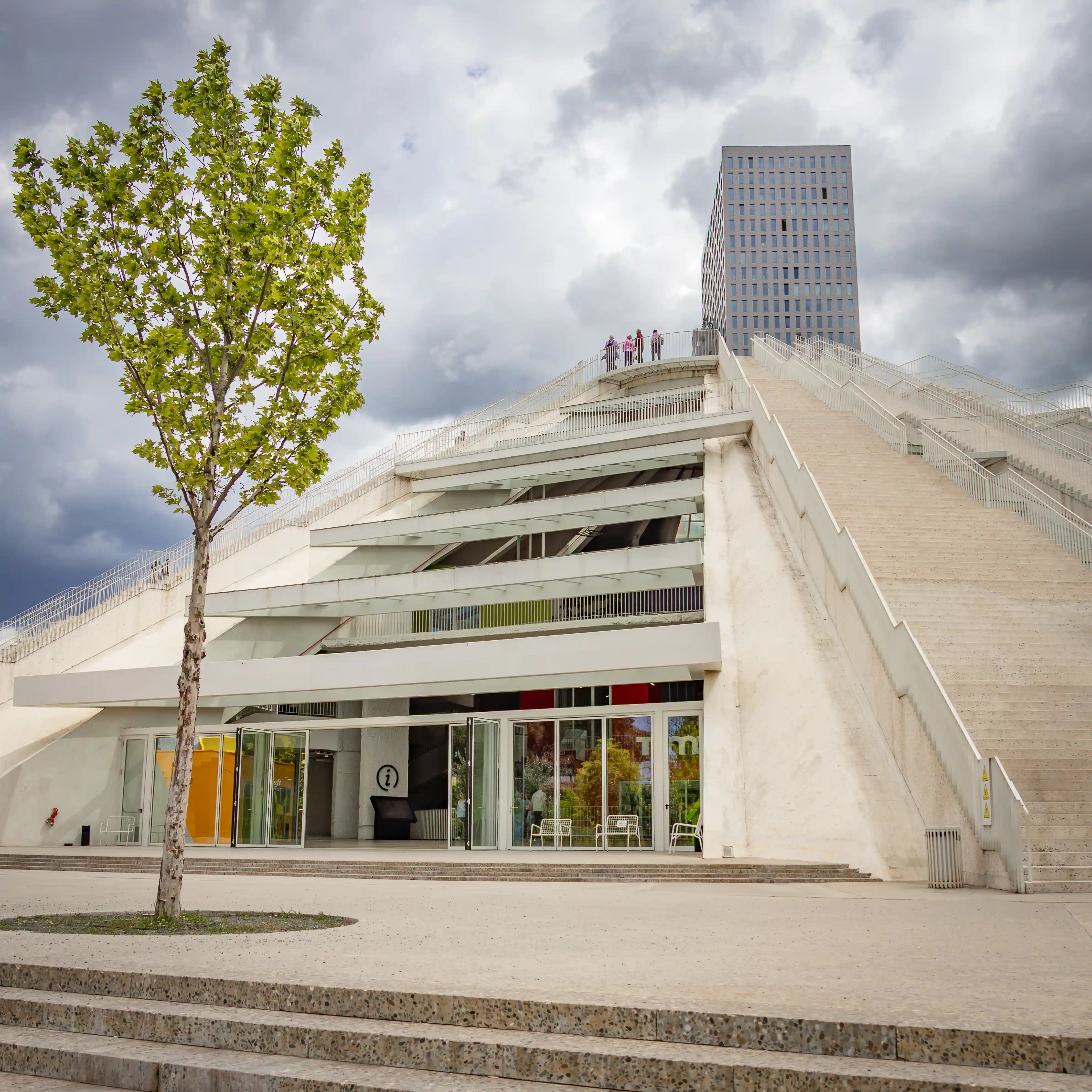 The renovated Tirana Pyramid with its exterior stairways and modern entrance beneath a dramatic sky.