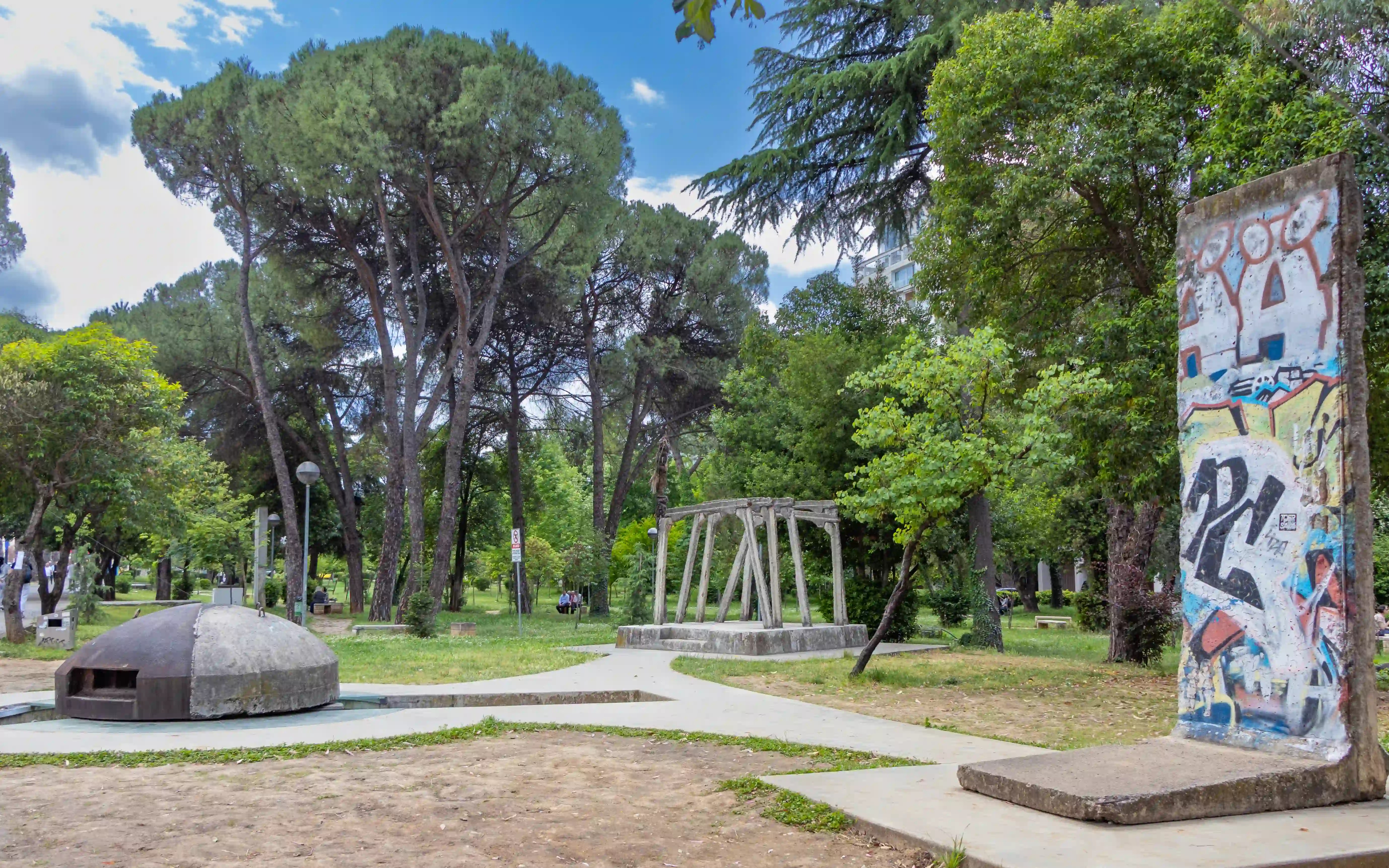 A preserved section of the Berlin Wall and a concrete bunker displayed at Postbllok memorial in Rinia Park, Tirana.