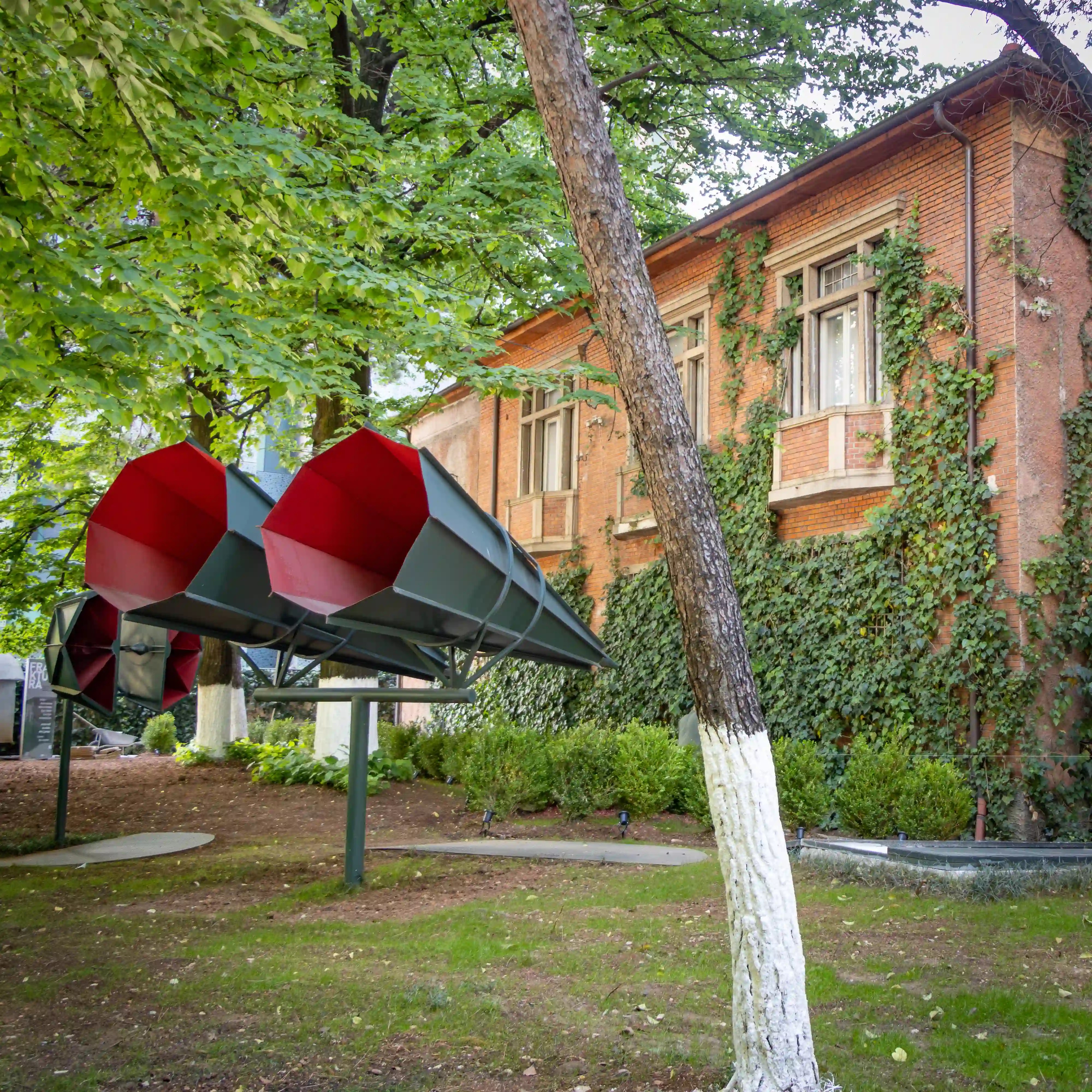 House of Leaves museum building surrounded by trees and a modern art installation in Tirana.