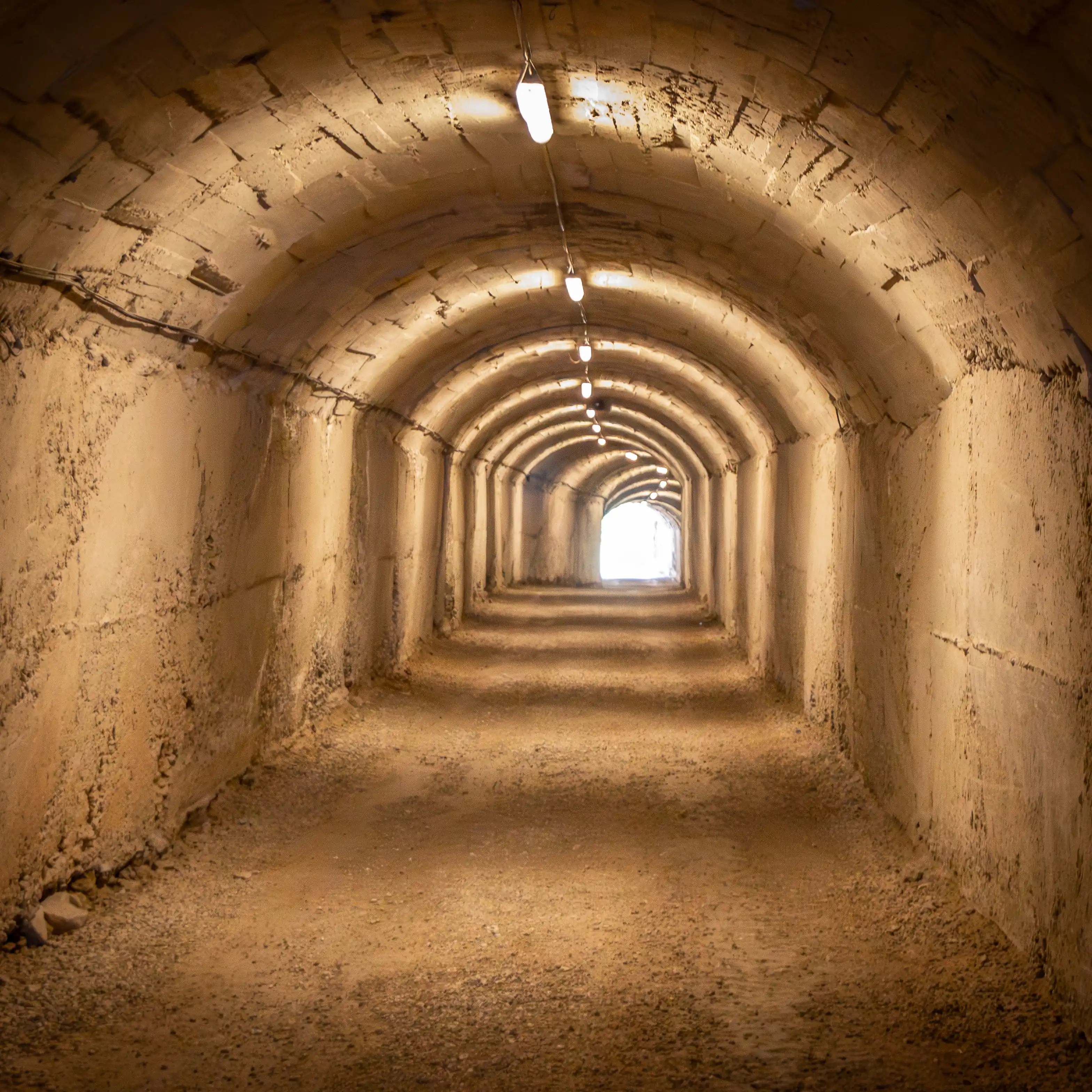 Concrete tunnel leading to Bunk'Art 1 illuminated by overhead lights.