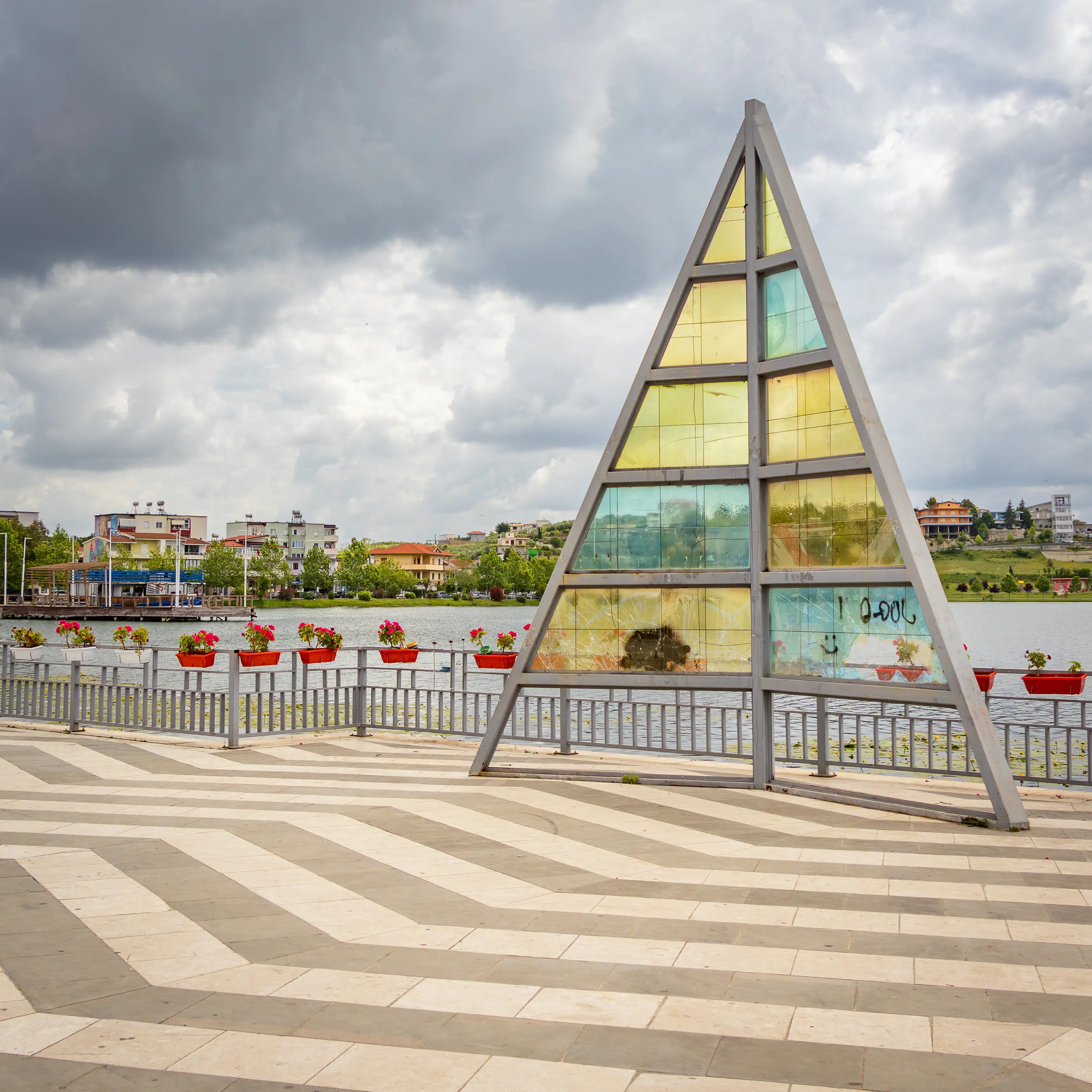 A triangular glass sculpture stands beside the promenade overlooking Belshi Lake.