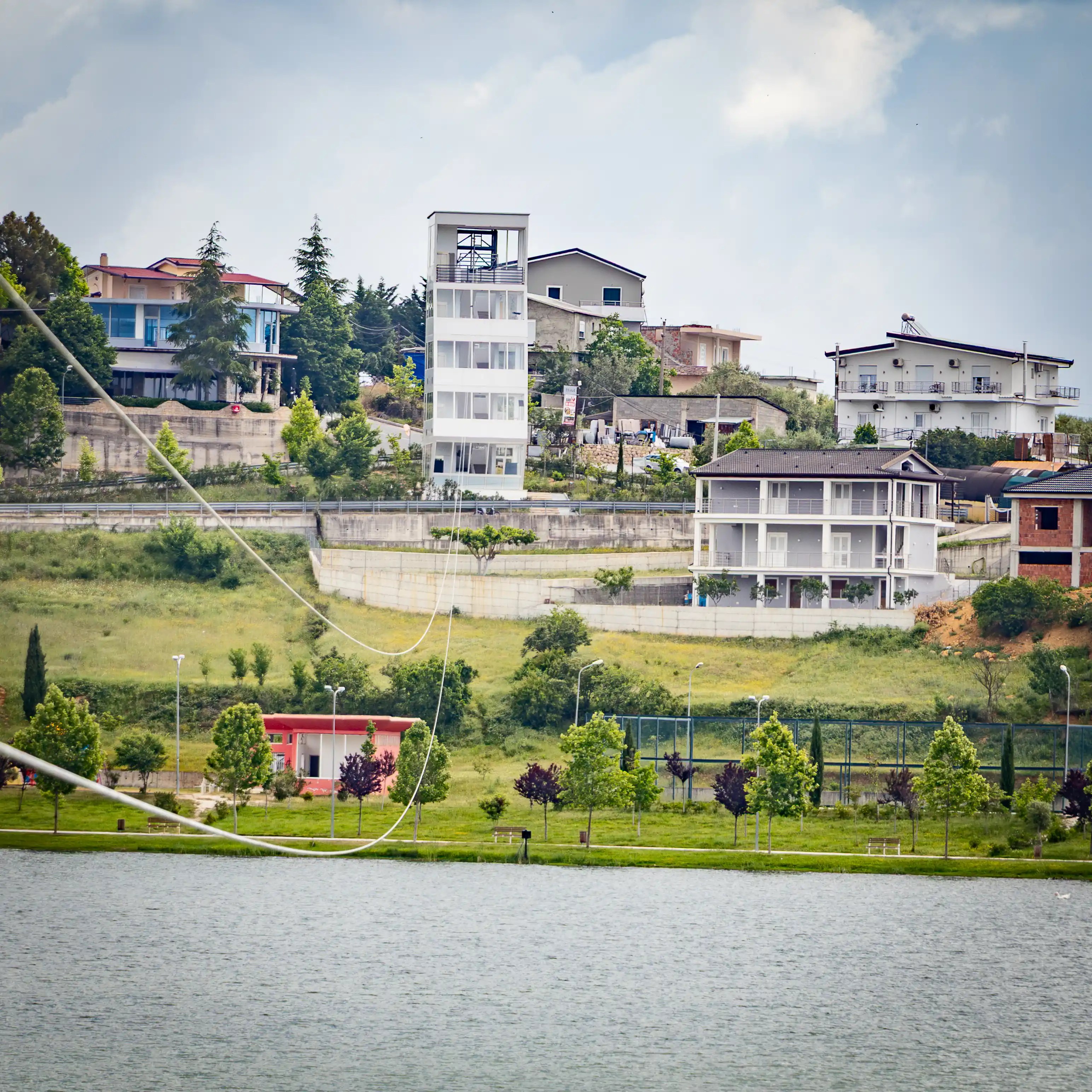 Homes and buildings dot a green hillside across Belshi Lake.
