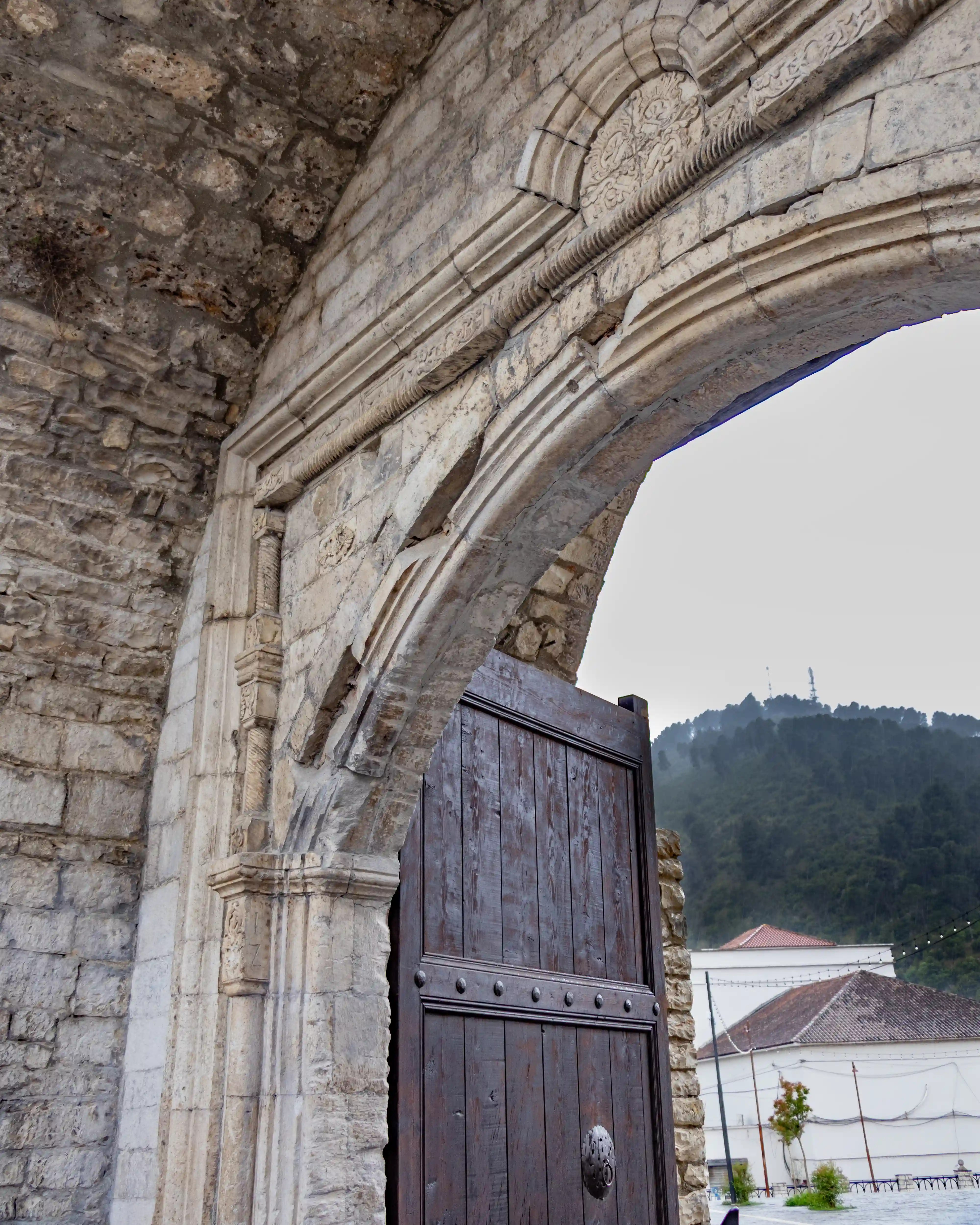 A carved stone archway and wooden door form part of the historic Gate of the Pasha in Berat Castle.