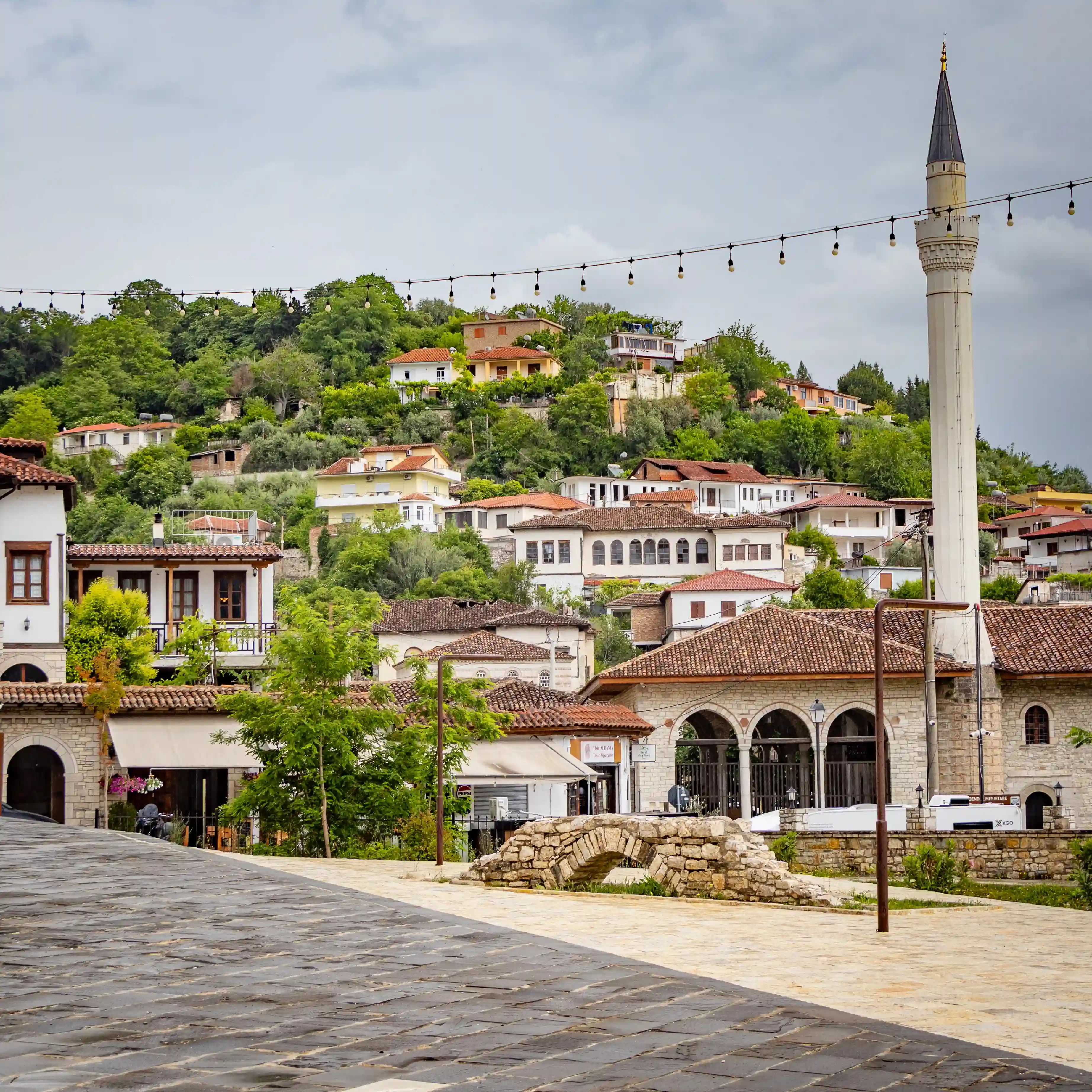 A mosque minaret rises above historic buildings with hillside homes in the background in Berat.