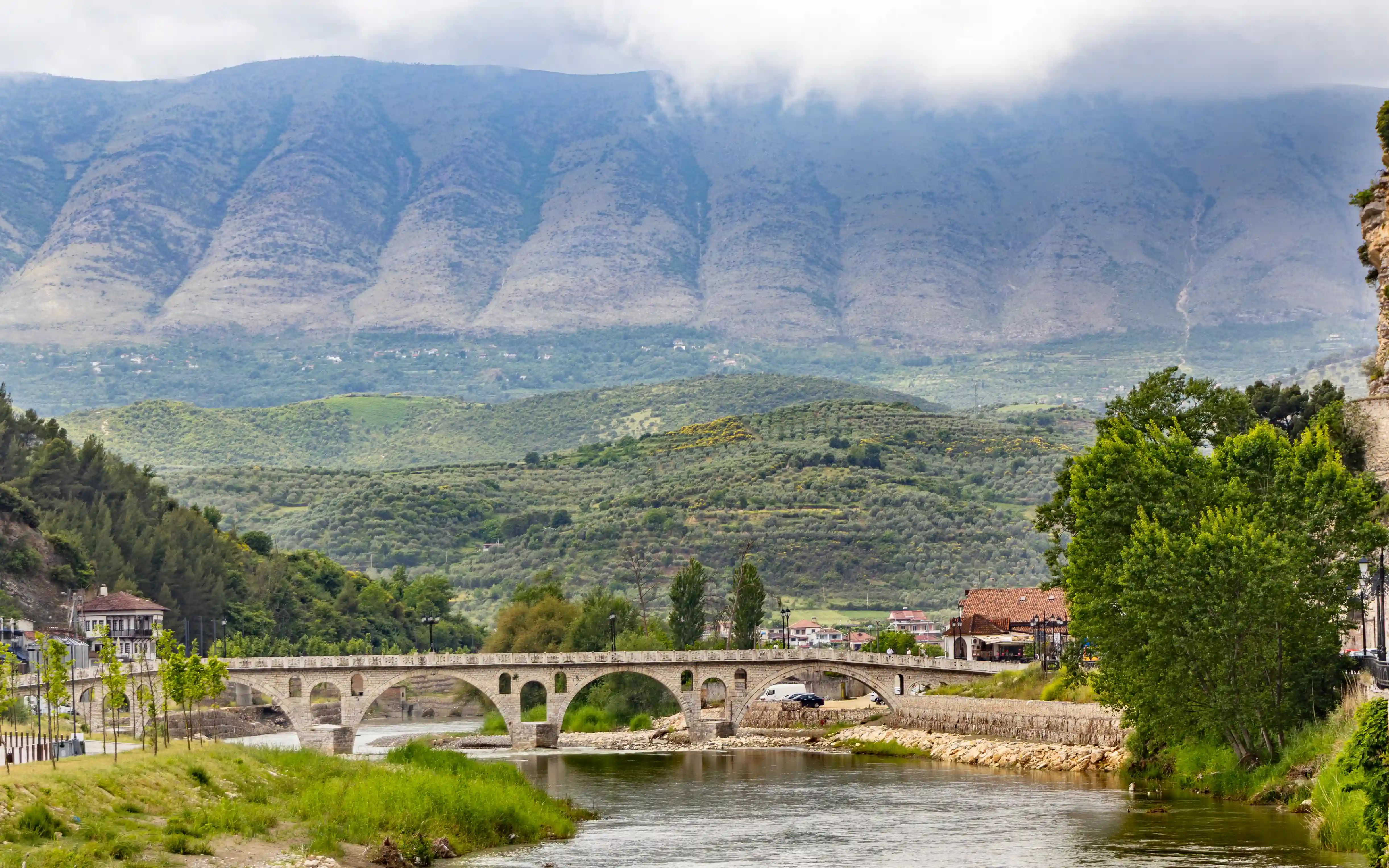 The stone arches of Gorica Bridge cross the Osum River beneath cloud-covered mountains near Berat.