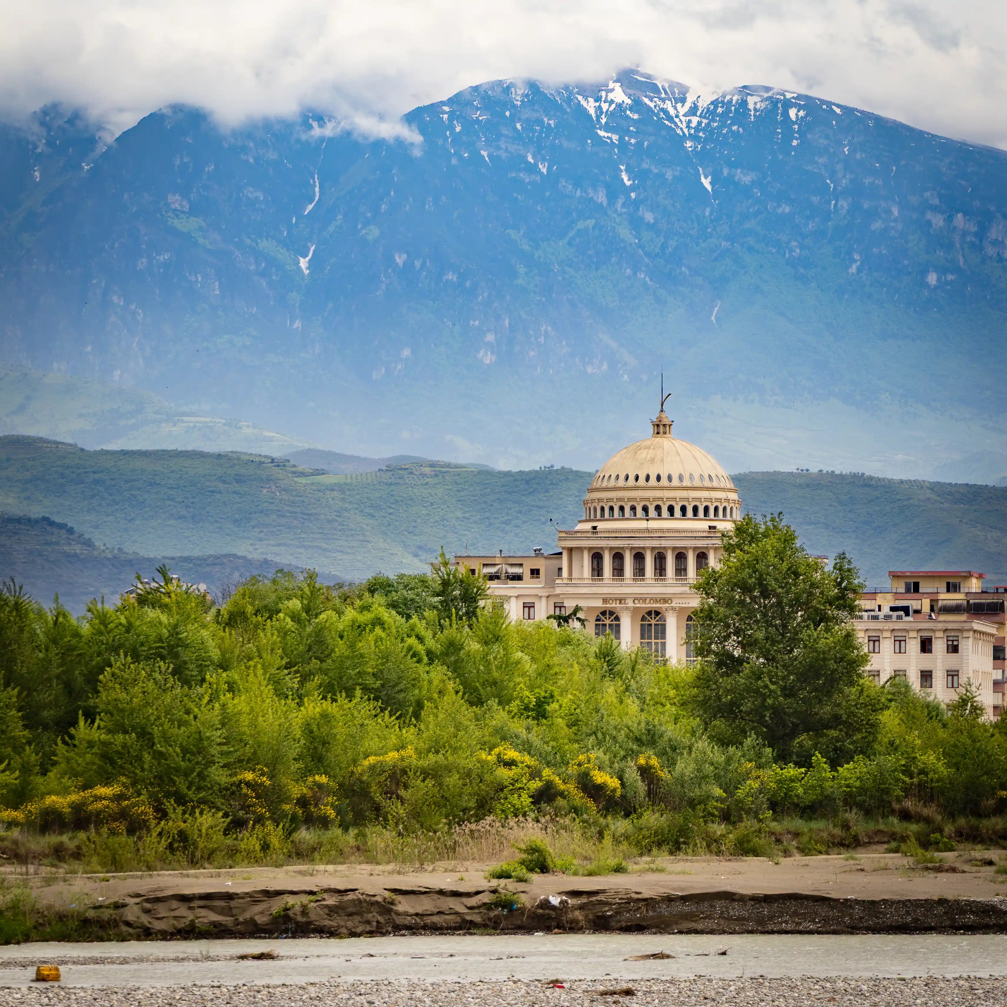 The dome of Hotel Colombo rises above trees with mountains and low clouds in the background.