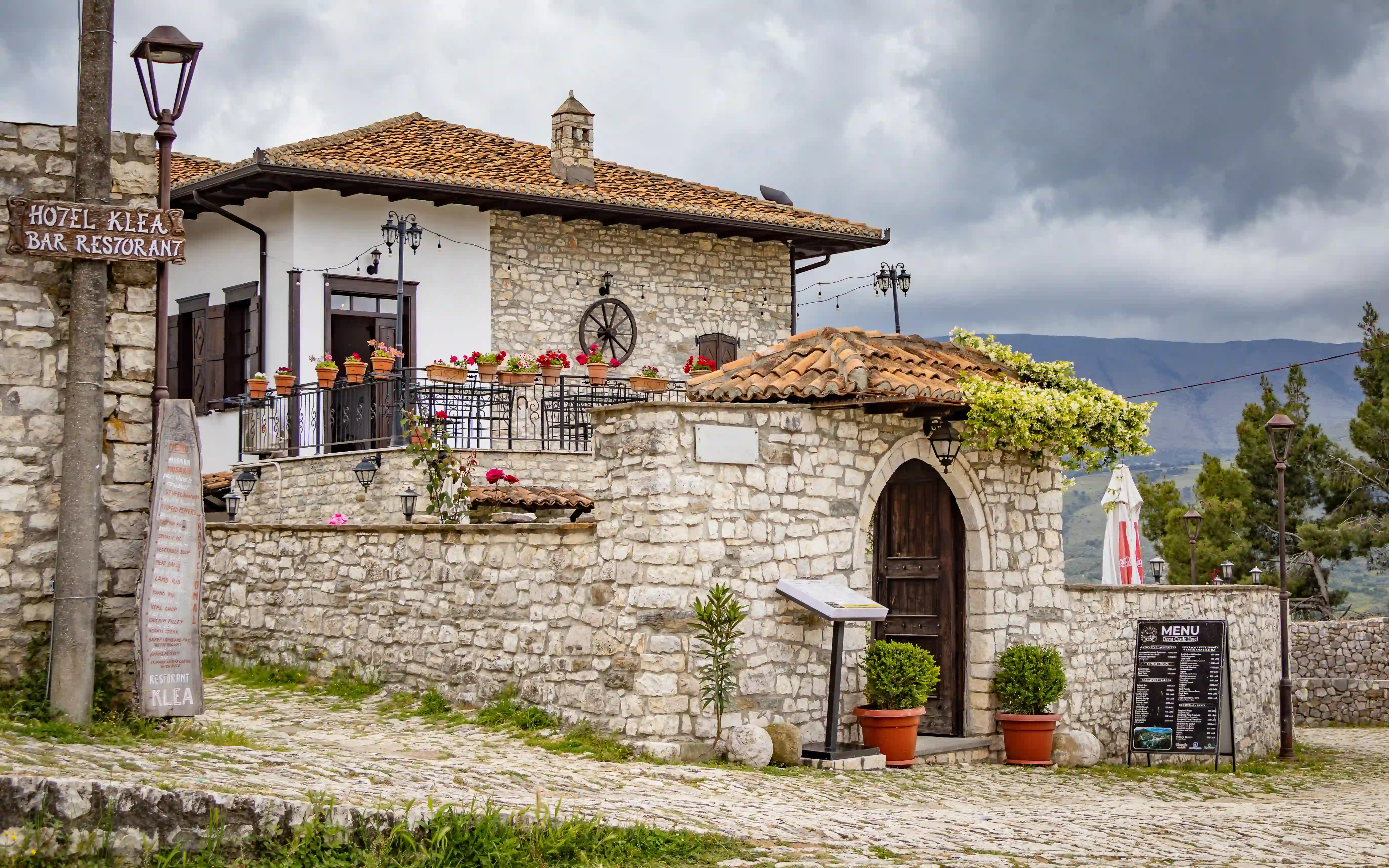 Traditional stone building with flower-filled terraces inside Berat Castle under dark clouds.