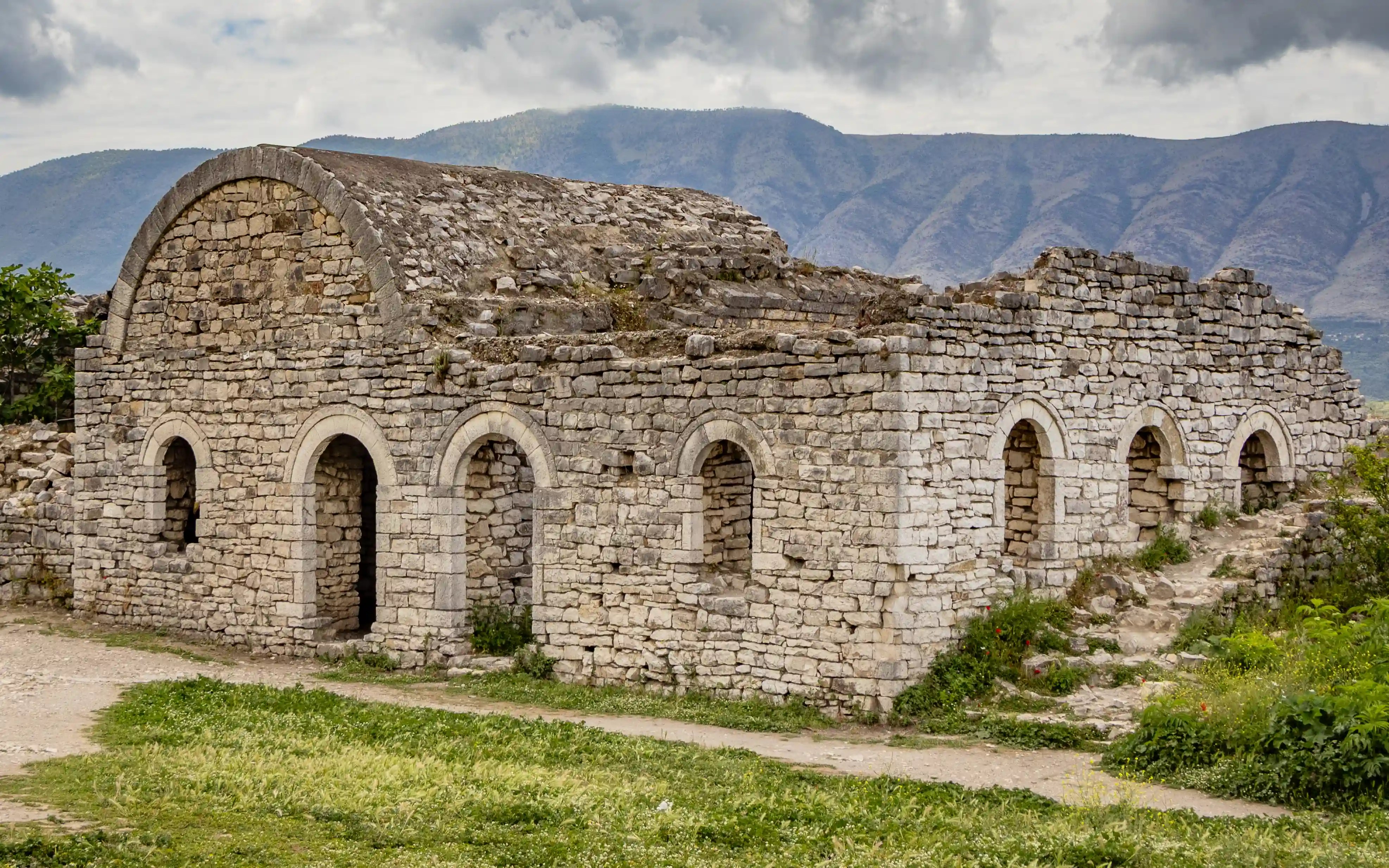 Stone ruins of a historic building inside Berat Castle with mountains beyond.