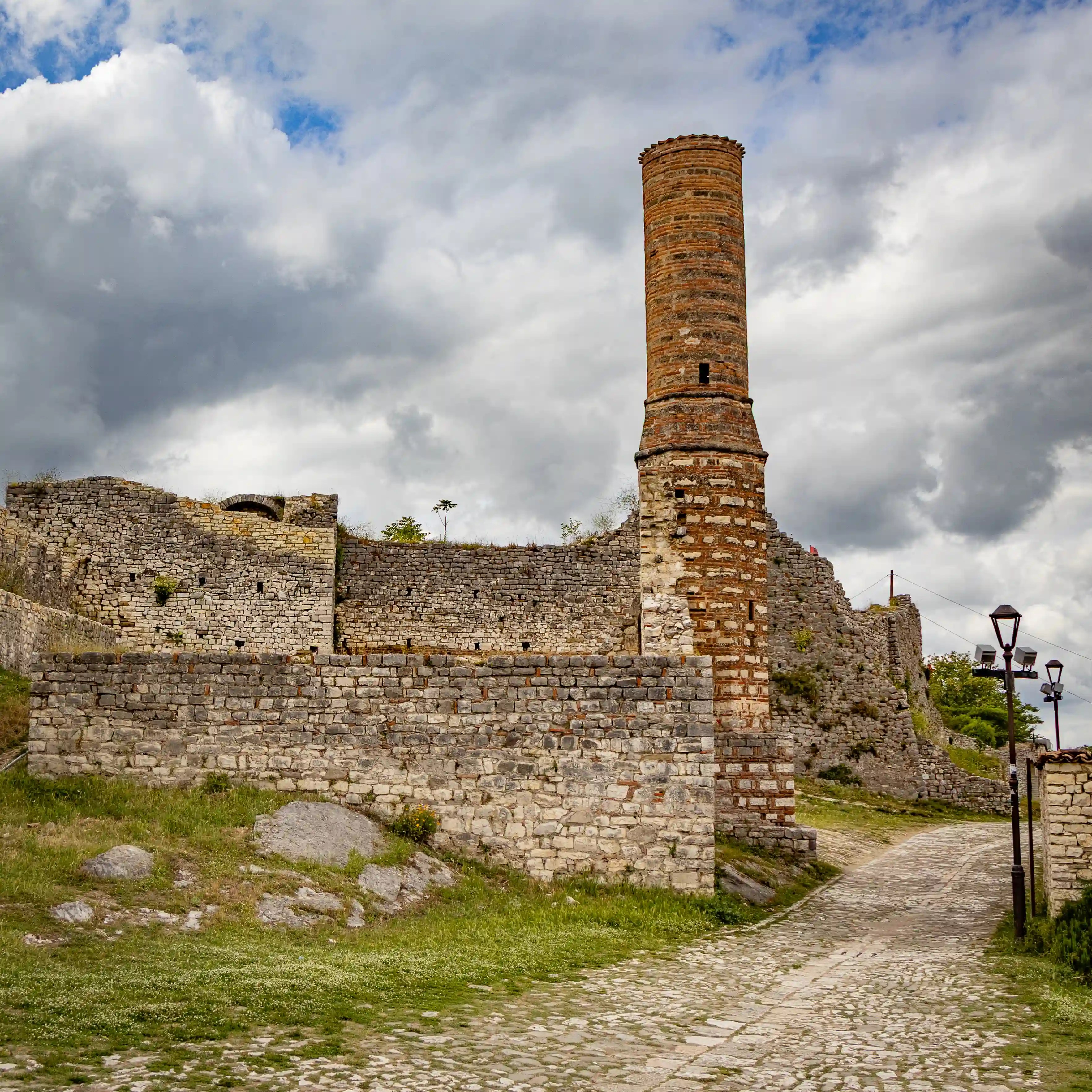 Tall brick tower rising beside the stone walls of Berat Castle.