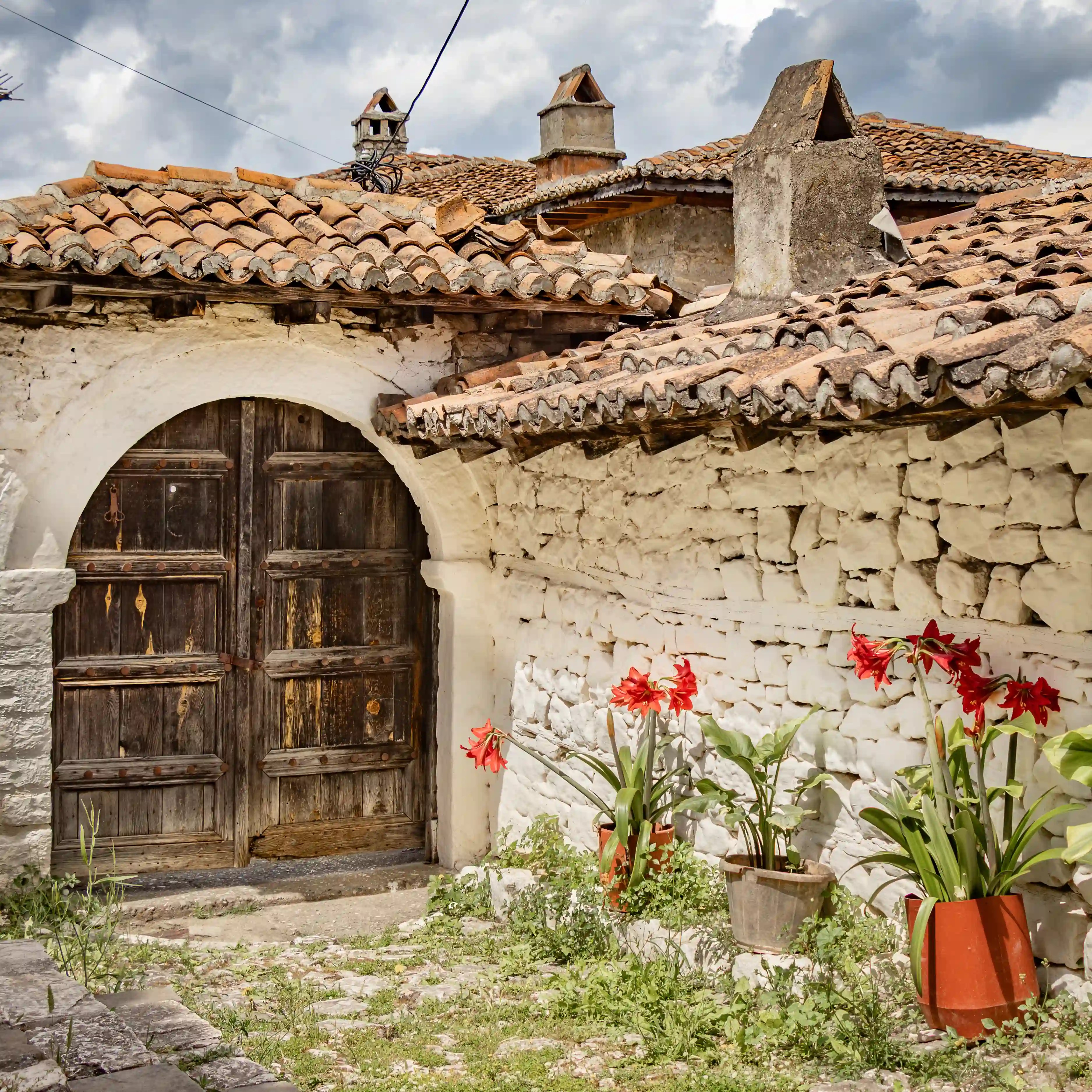 Traditional stone house with a weathered wooden door and red flowers in pots.