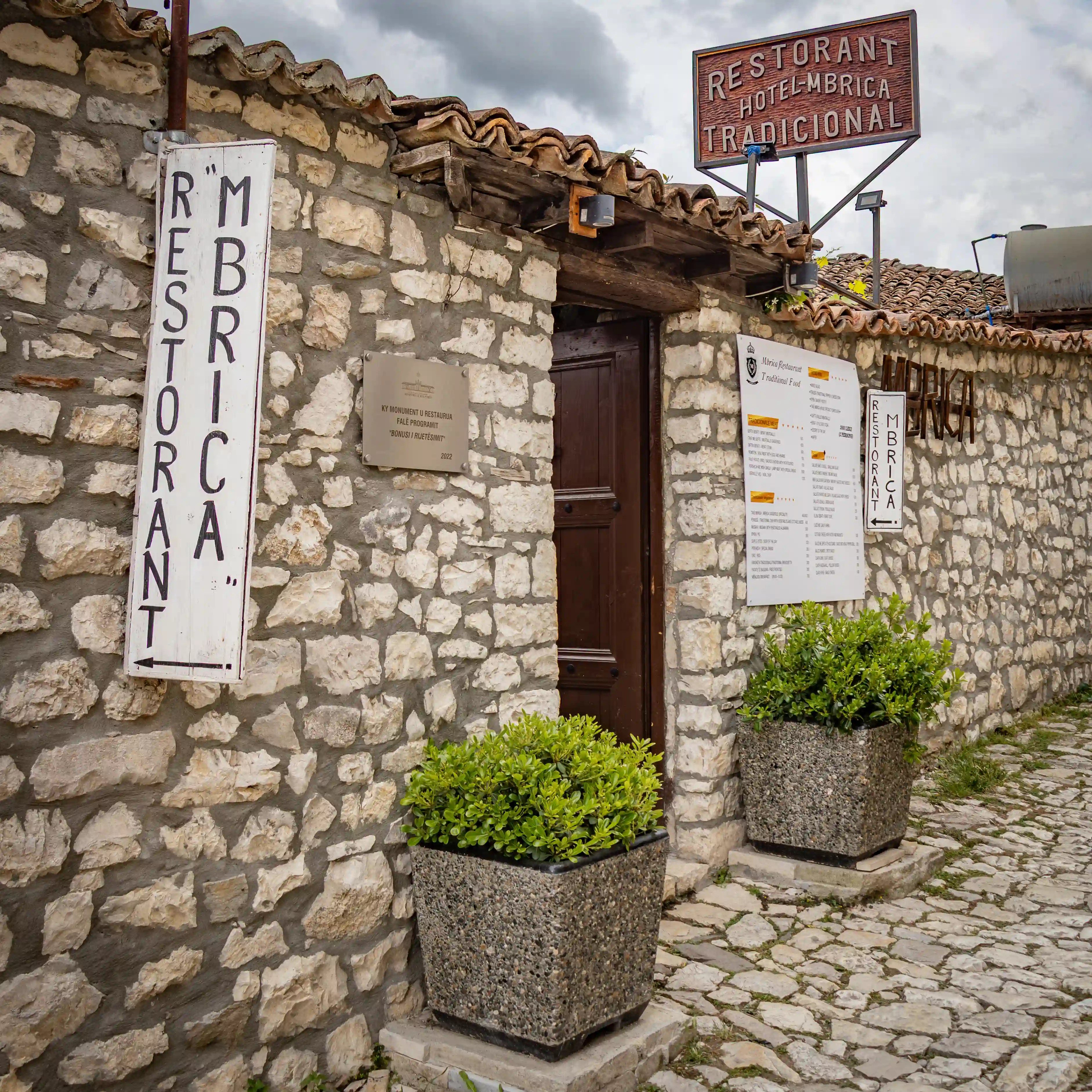 Stone building with signs for Hotel Mbrica and its traditional restaurant.