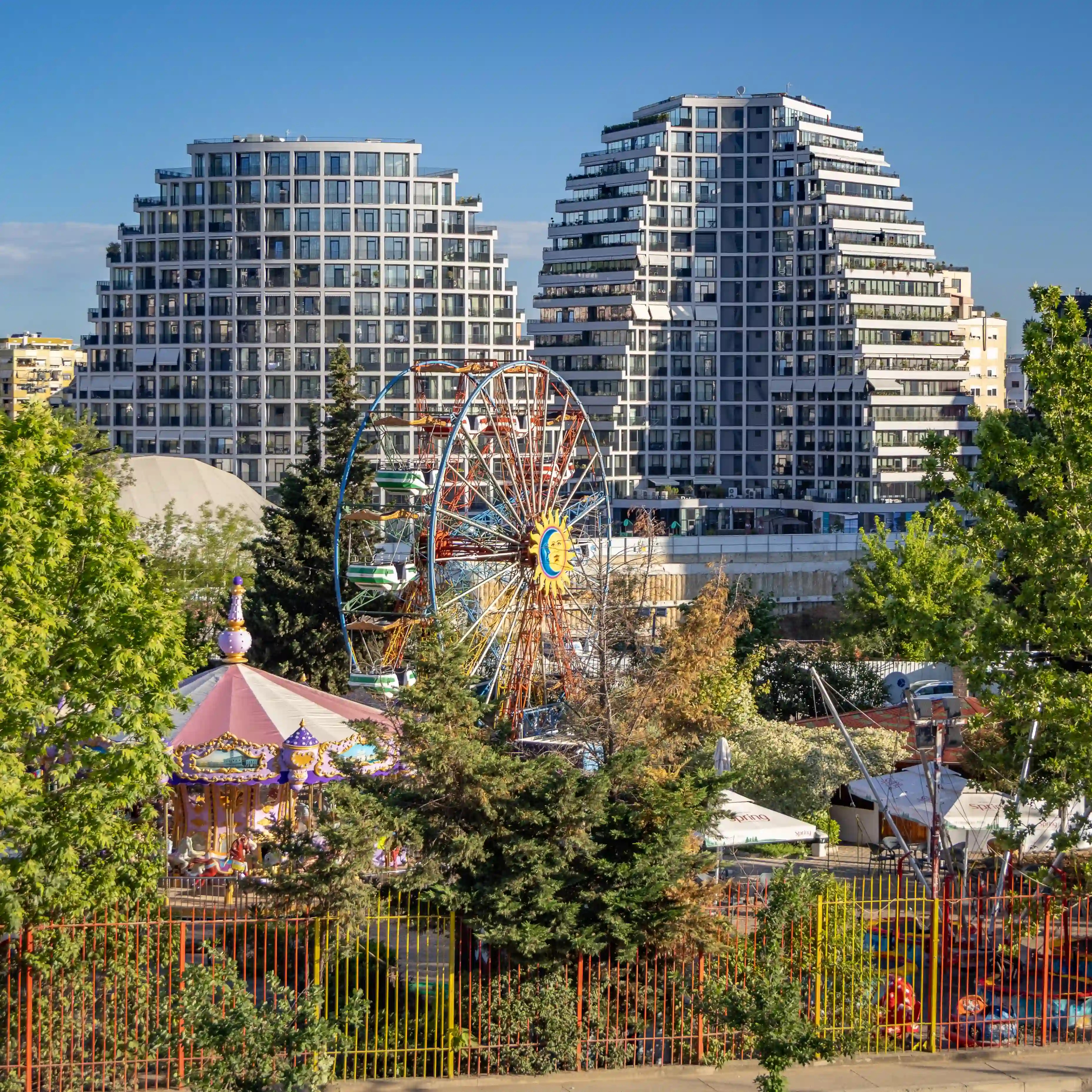 A Ferris wheel and amusement rides near modern apartment buildings beside Tirana's Artificial Lake.
